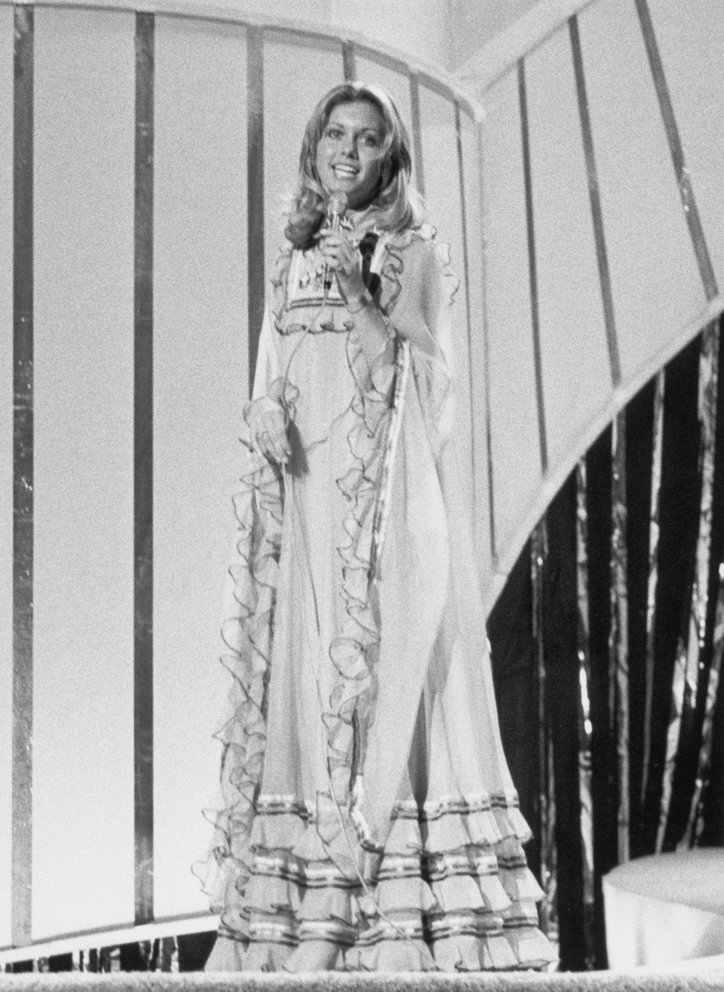 Olivia singing on stage in a floor length ruffled and tiered prairie dress