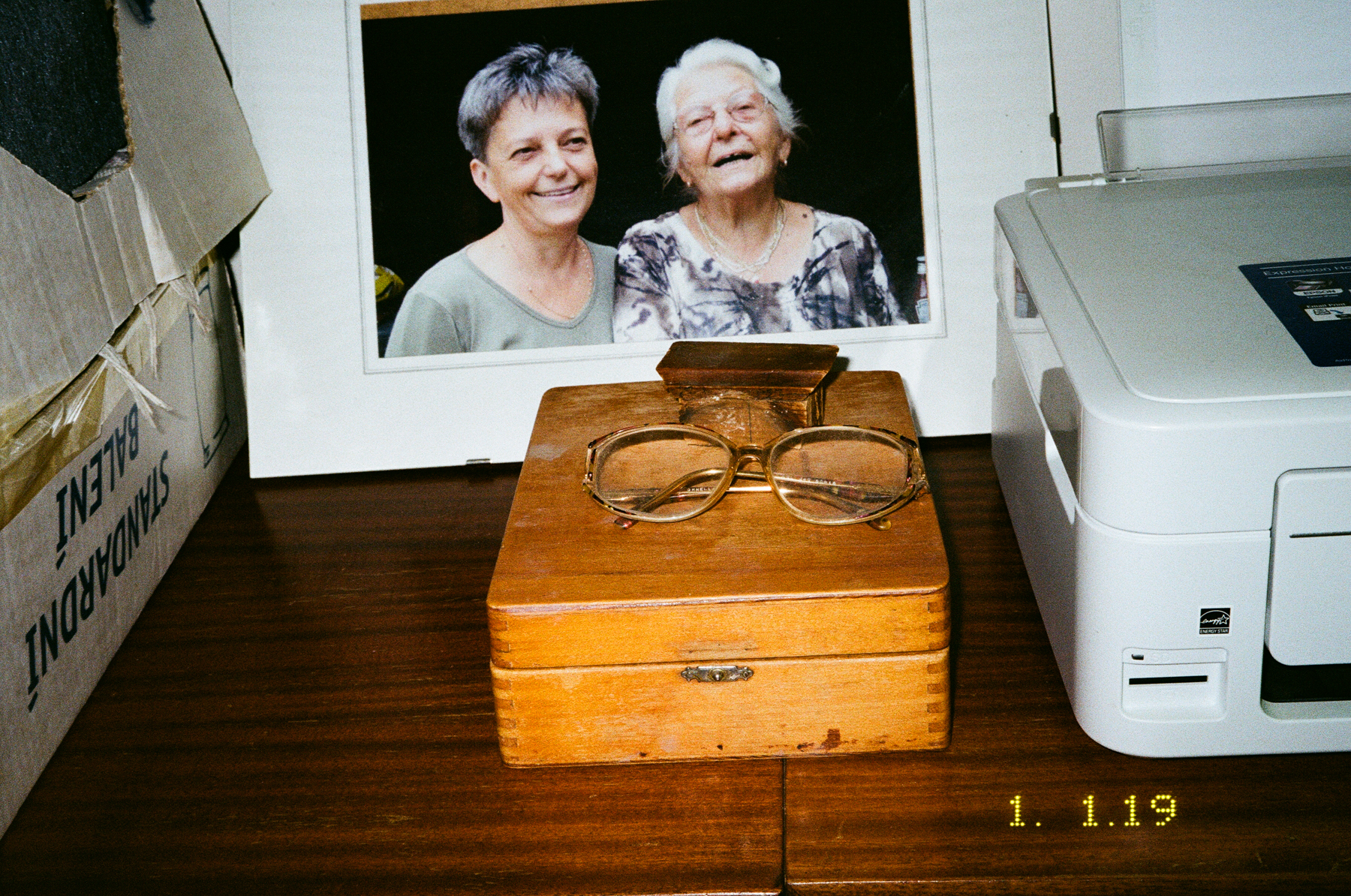 Photograph by Marie Tomanova of a photograph on the wall of her mum and grandma along with a wooden box, a printer and a pair of glasses