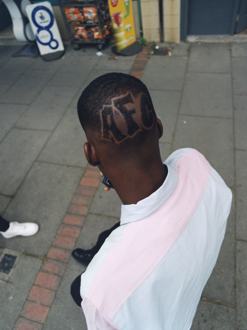 School kid in a shirt with a buzz cut standing on the street photographed by Bolade Banjo in i-D's The Ultra! Issue, no.369, Fall 2022