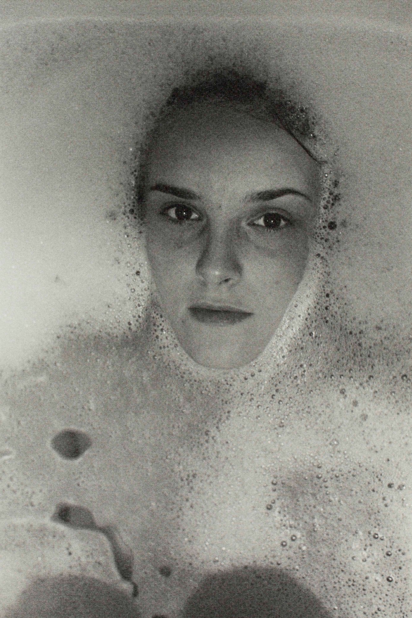 black-and-white image of a woman in a bubble bath, only her face can be seen above the water