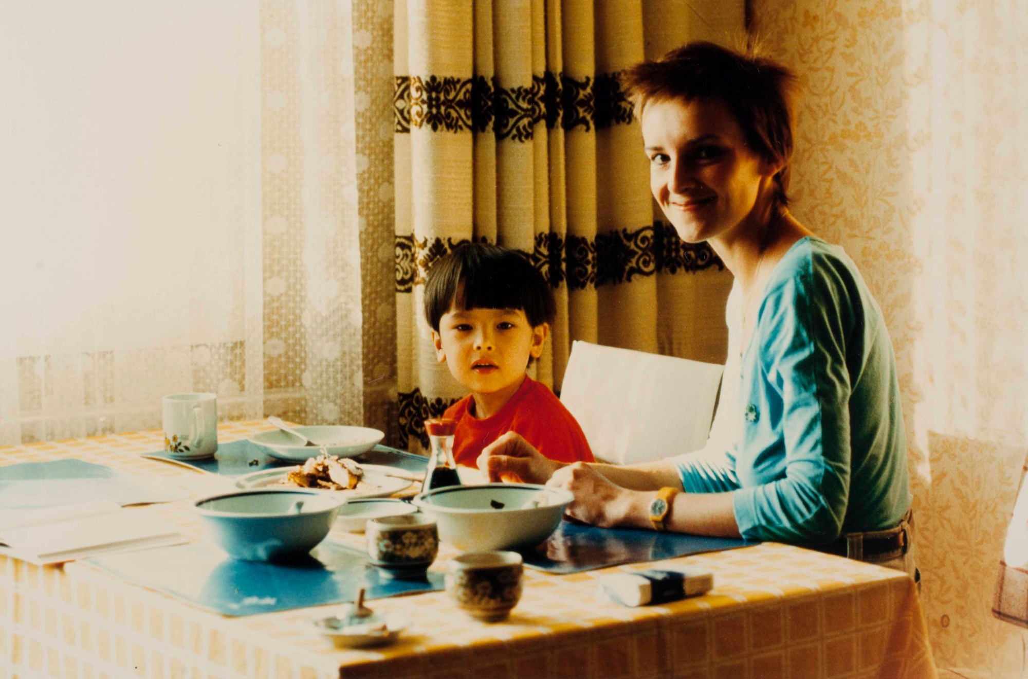 a woman and a toddler sitting at the breakfast table, the woman smiles over her shoulder at the camera