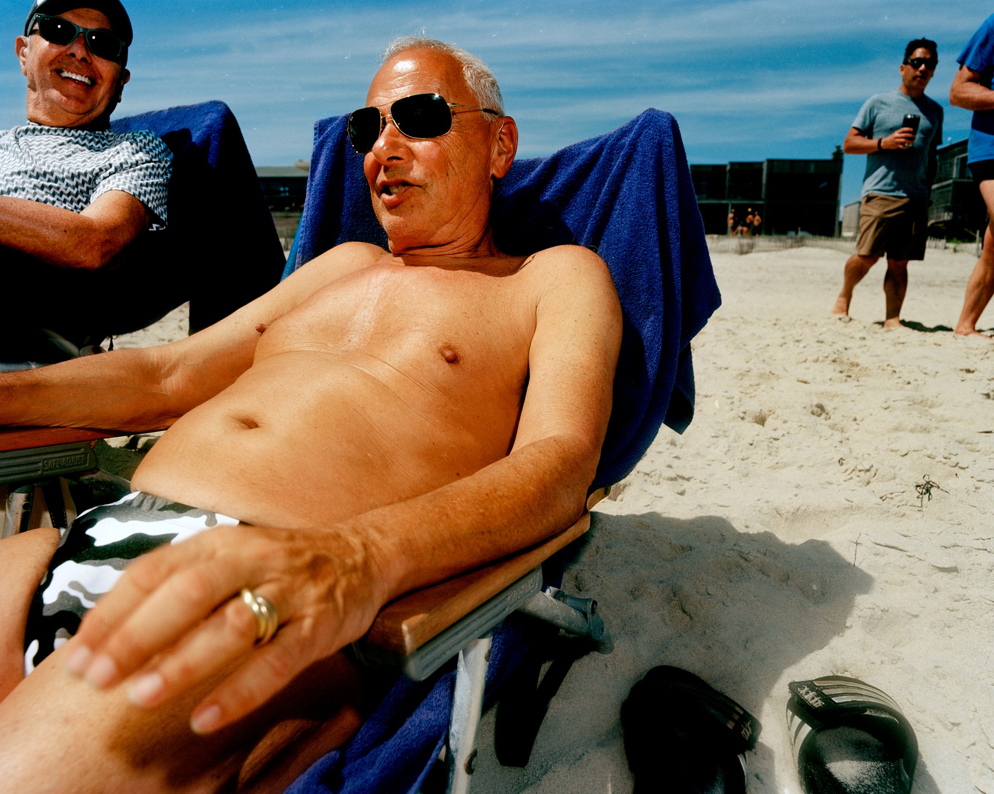 a man wearing camo speedos lounges in the sun at a gay beach