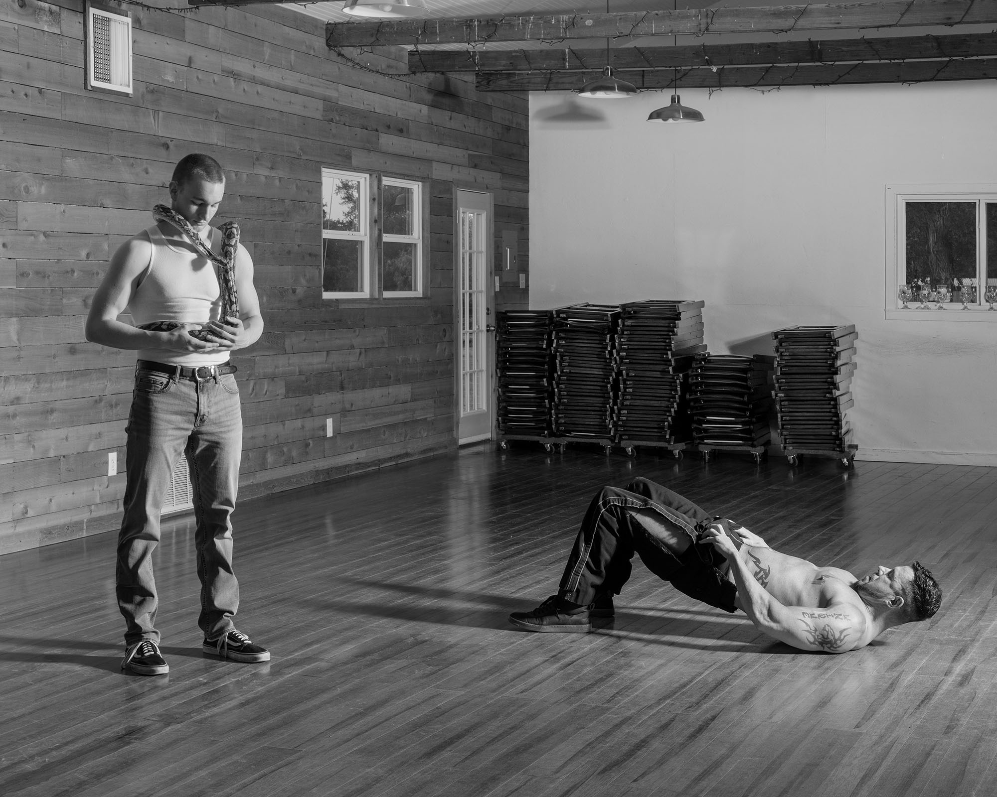 two muscular men in a church basement, one with a snake round his next, the other lying down shirtless