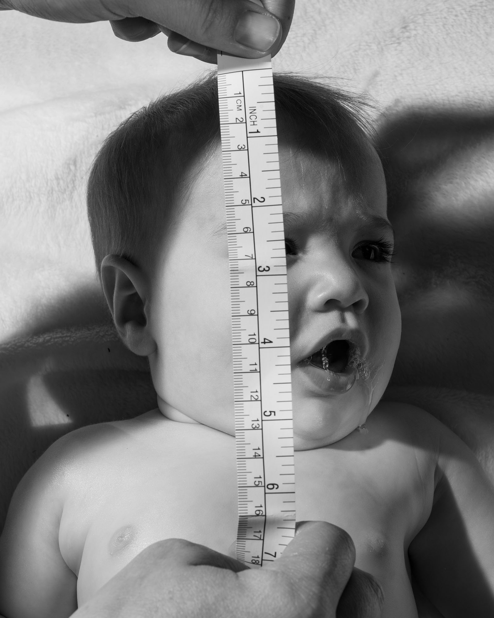 a baby gurgling with a measuring tape held above their face