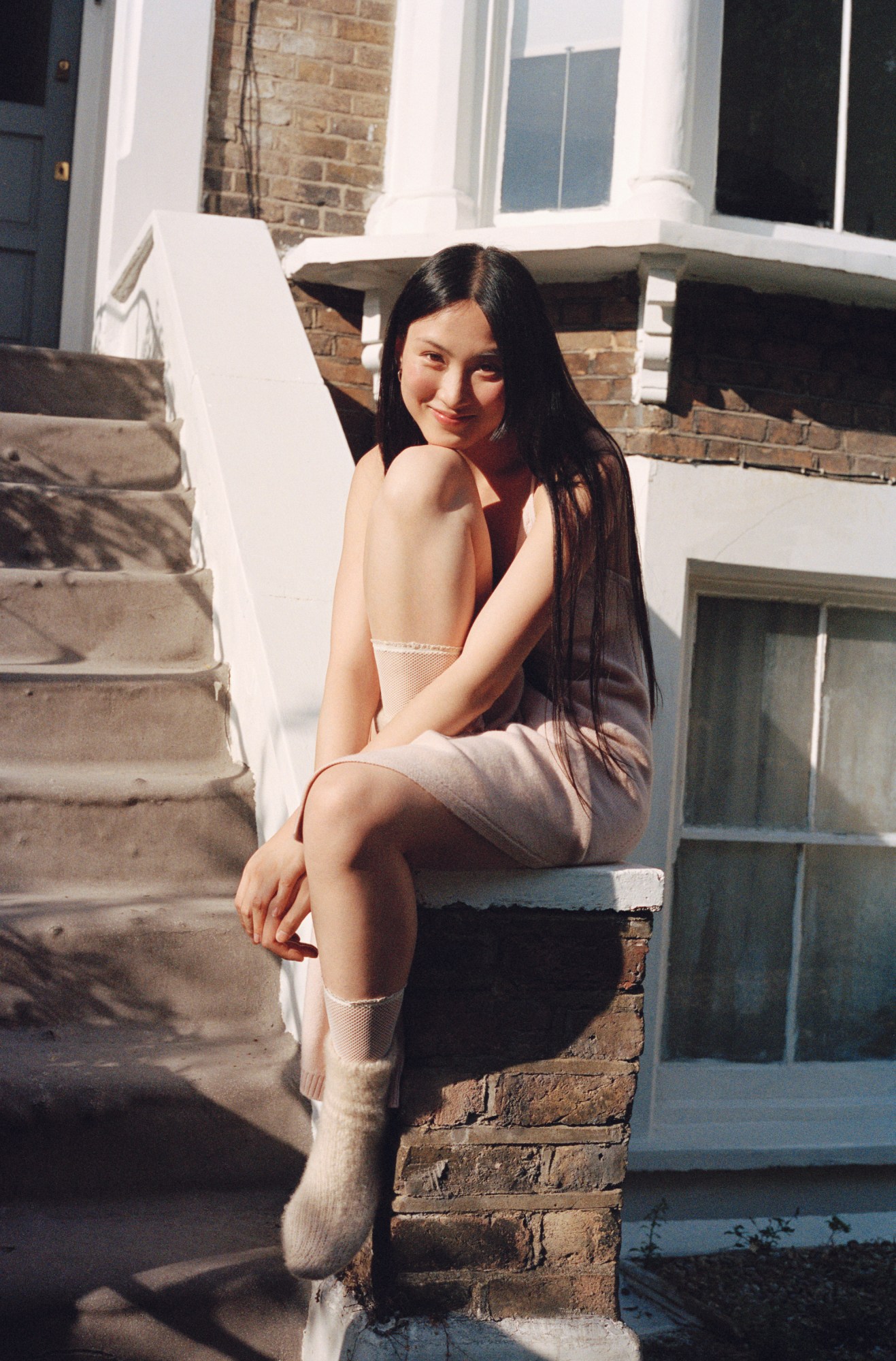 Woman sitting on a brick wall outside a flat wearing Loro Piana cocooning collection