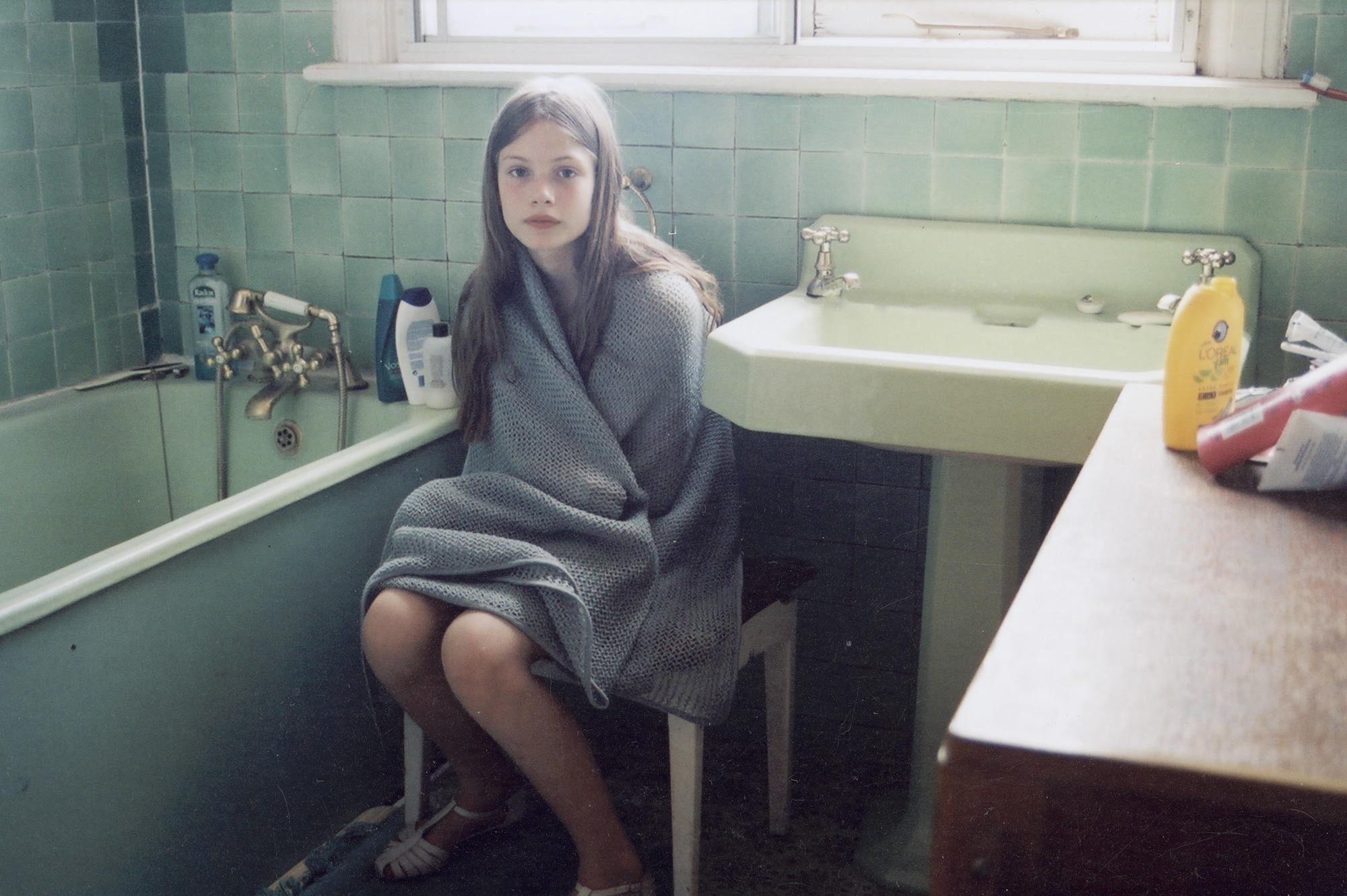 sylvia shot by angela hill in a green bathroom sitting on a white chair wrapped in a grey towel