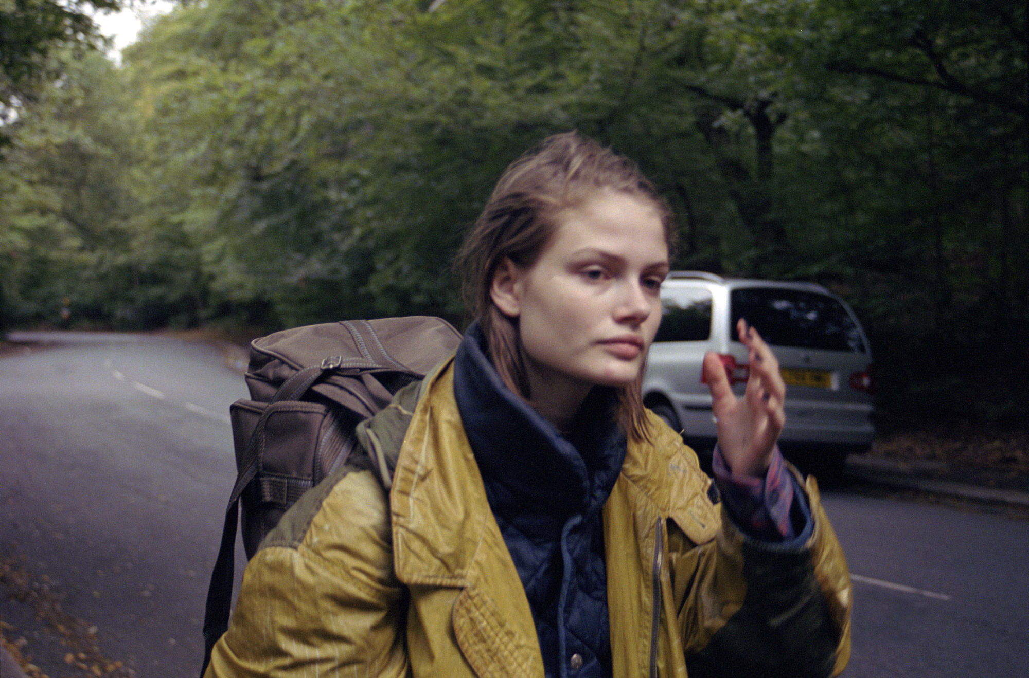 sylvia shot by angela hill wearing a yellow leather jacket walking along the side of a road in the woods