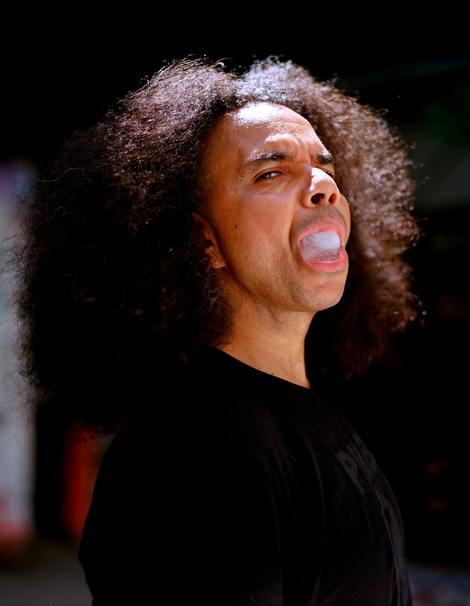 a person with an afro looks to the camera holding a large ice cube in their mouth