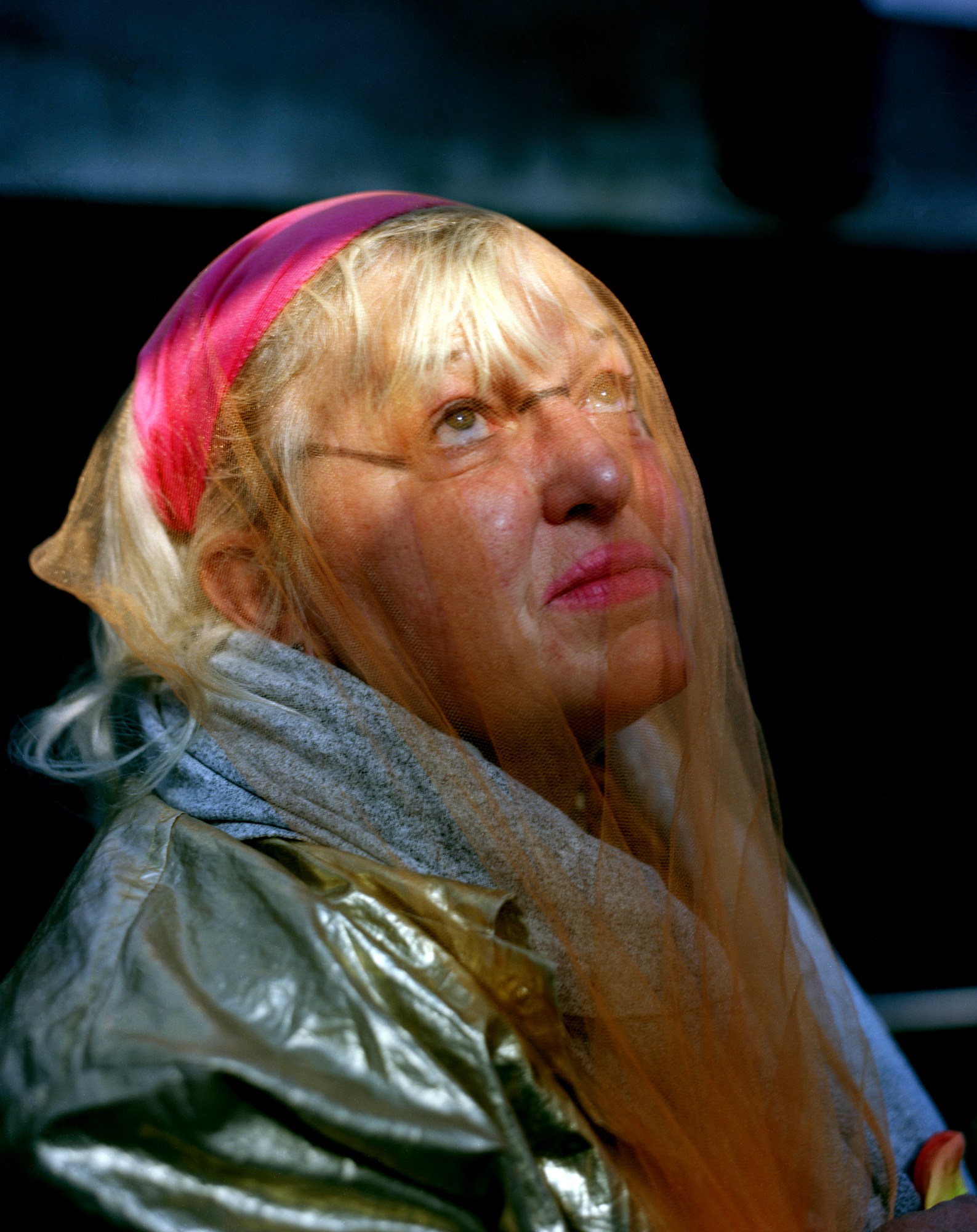 a person with blonde hair and bold pink lipstick wears a shimmery orange veil over their face