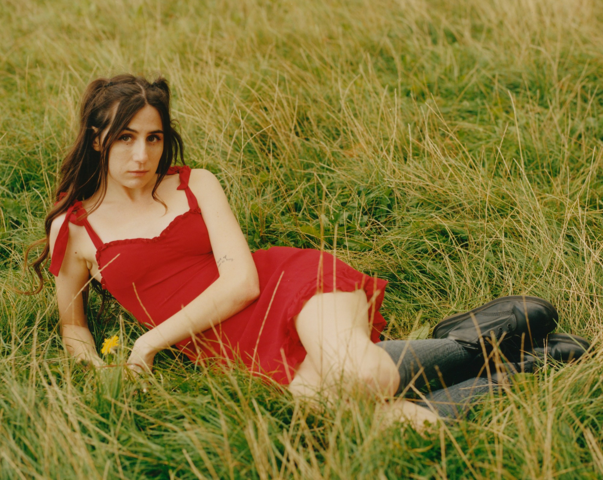 dodie lying in a field of grass, wearing a bright red dress