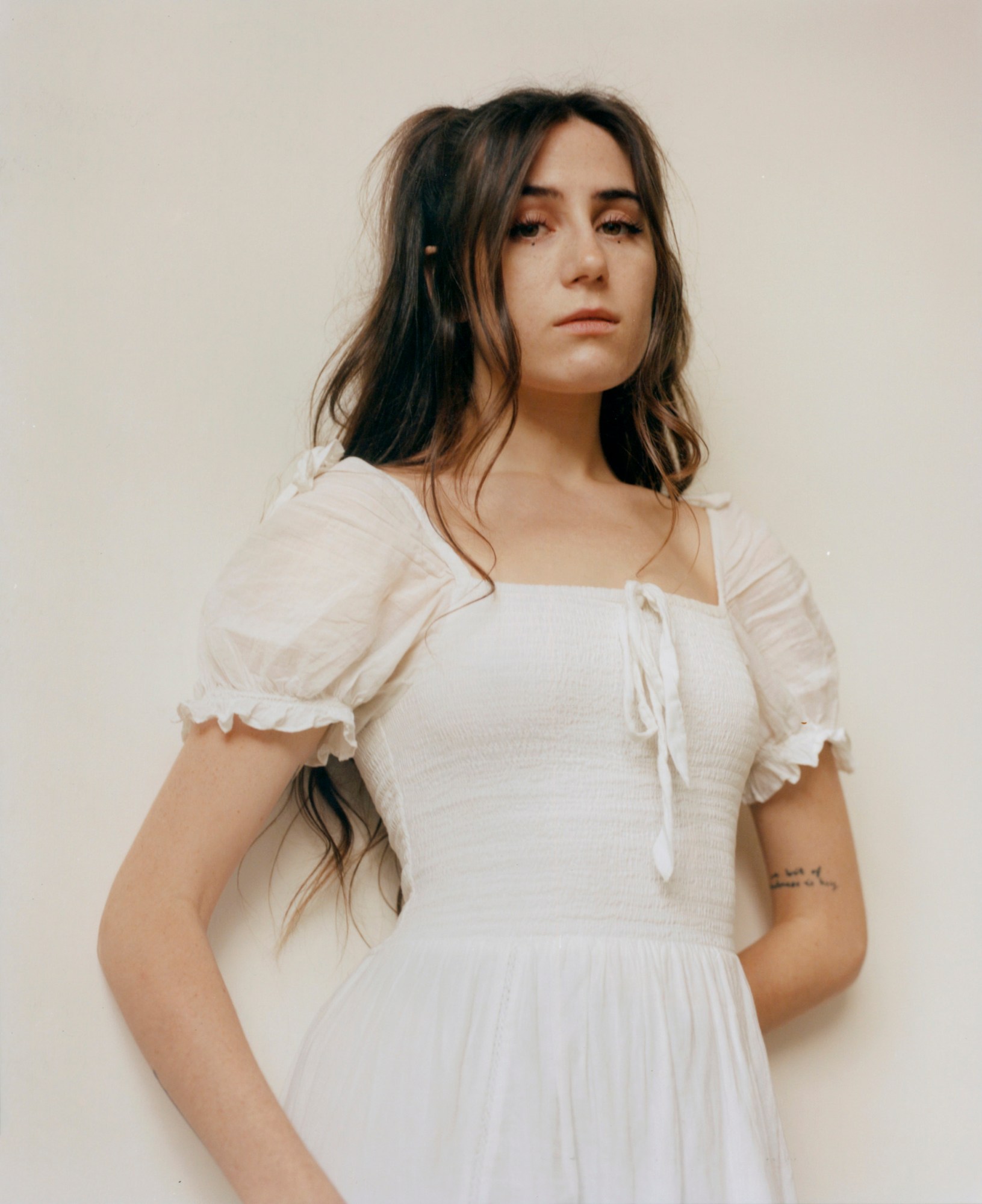 a portrait of dodie in a white dress standing against an off white background