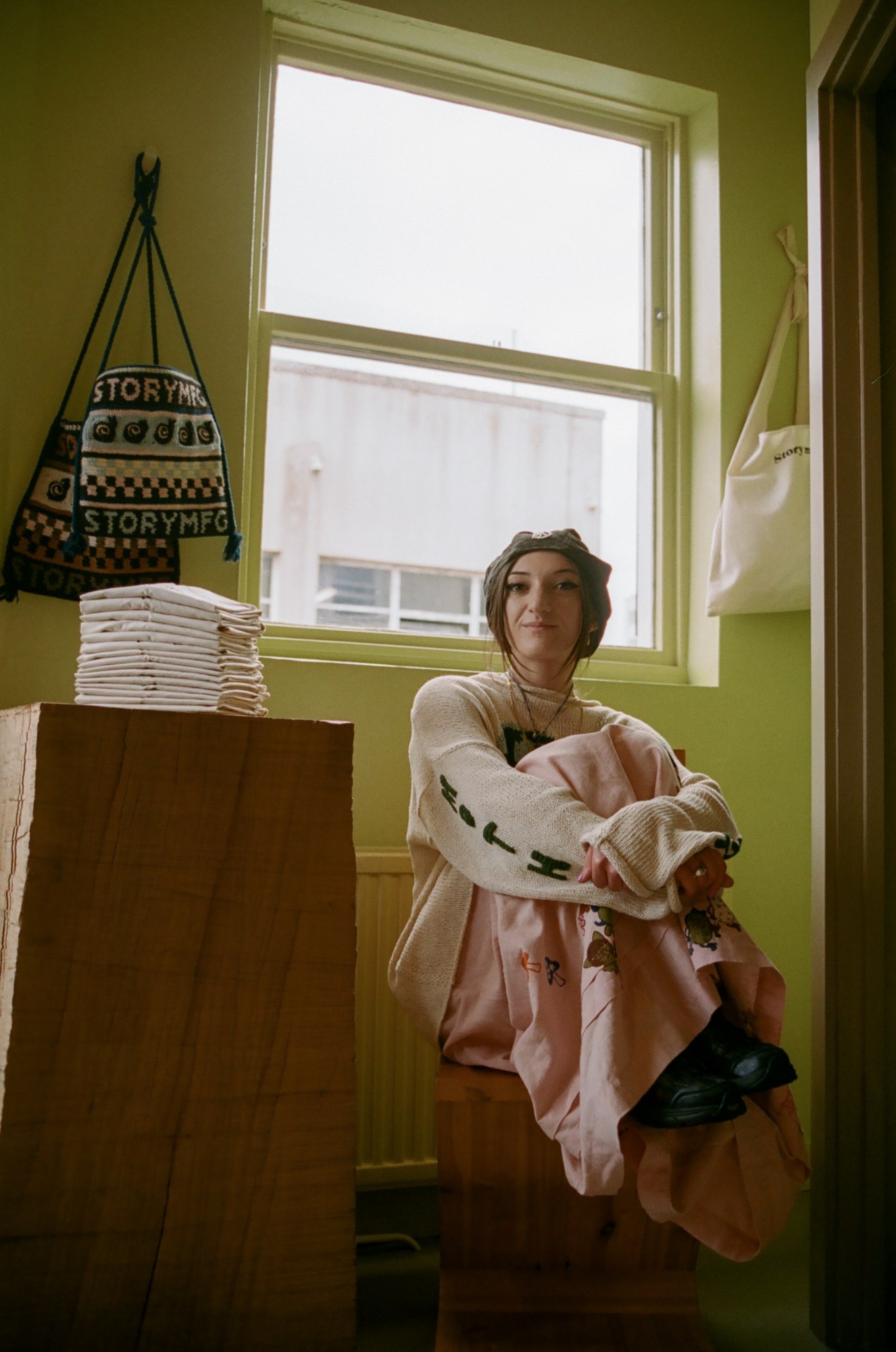 a woman in a long pink dress sits on a wooden chair, holding her knees to her chest