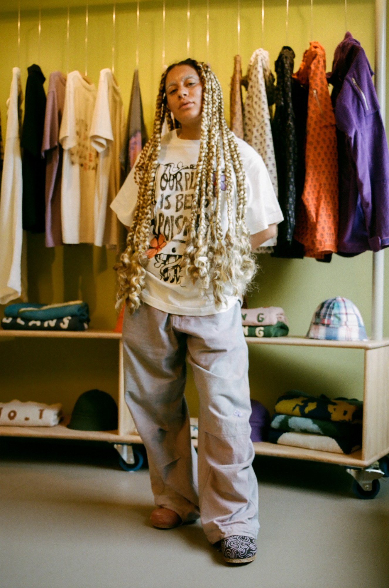 somebody with long blonde braids stands in front of a clothes rail