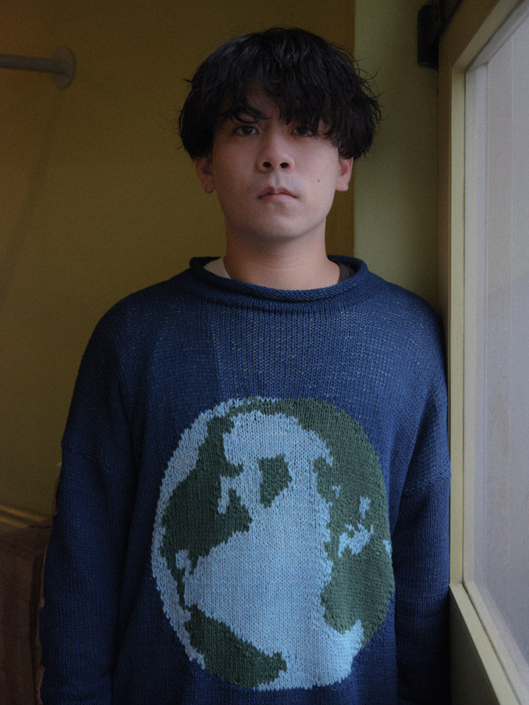 a man stands by a window wearing a navy sweater with a globe on it