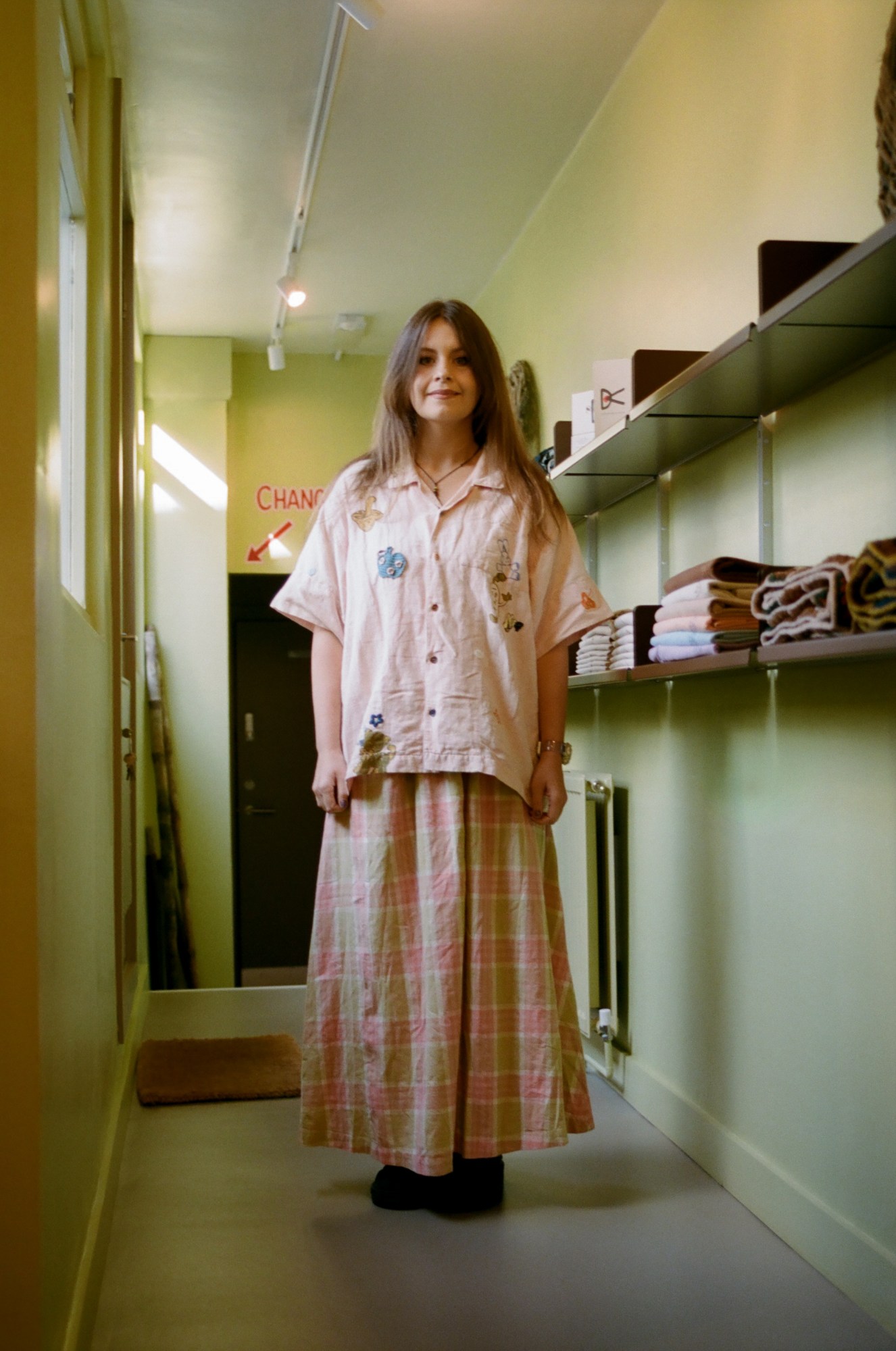 a brunette woman wears a pink shirt over a long checked dress