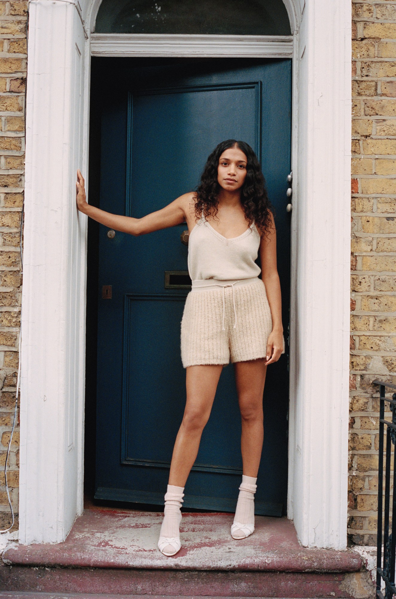 Woman stands against blue door frame on street in Loro Piana cocooning collection