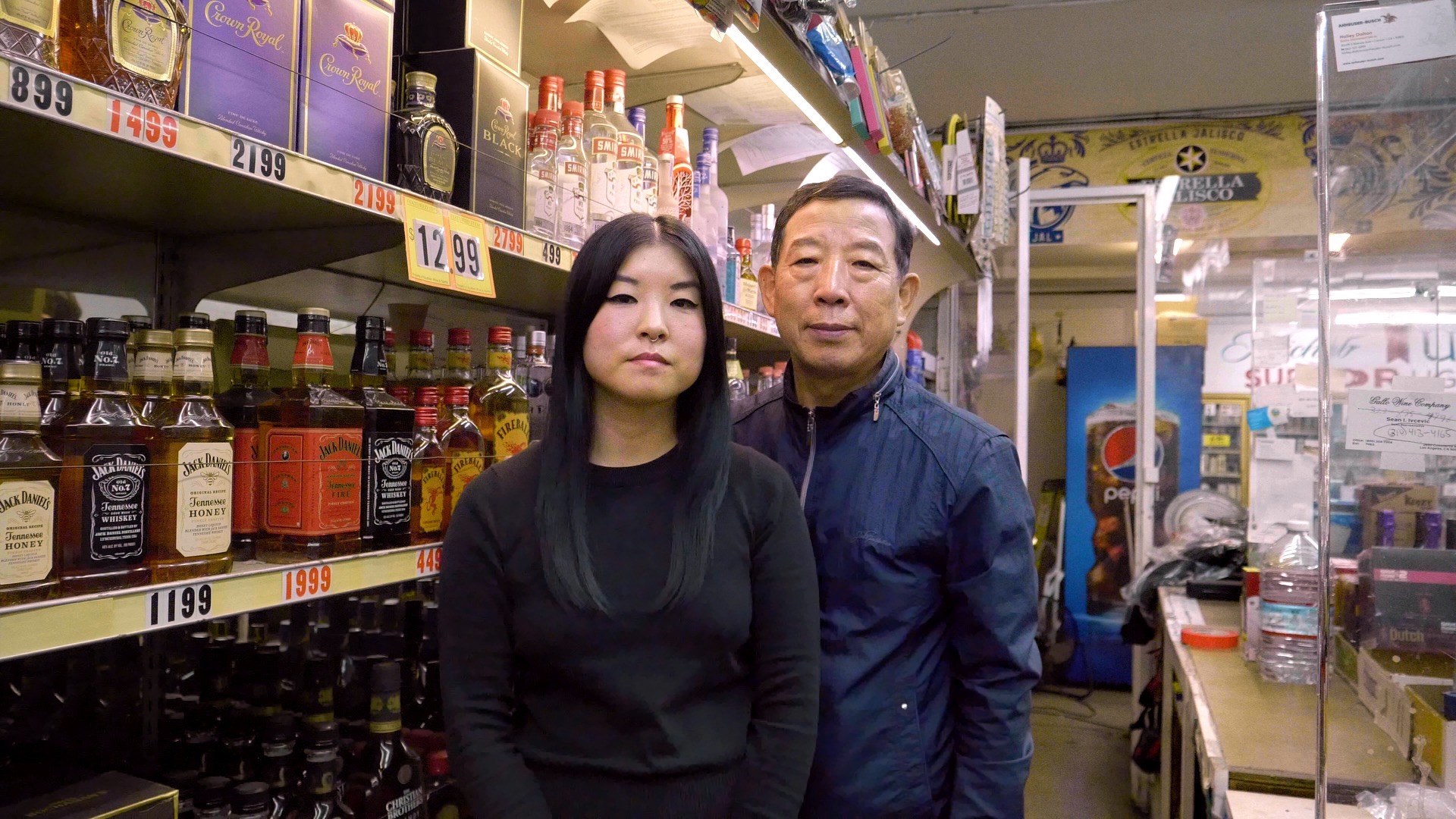 Still from Liquor Store Dreams (2022) showing two people in a liquor store in front of alcohol shelves