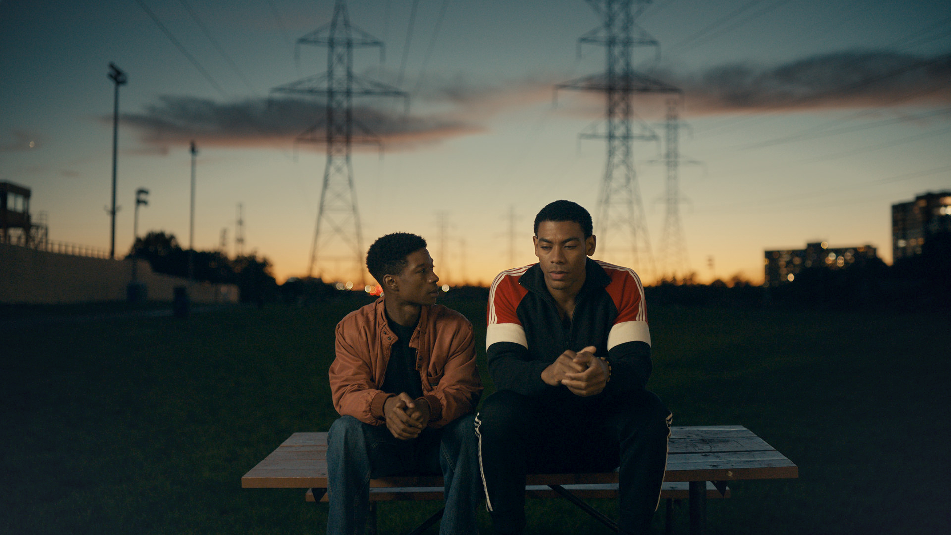 A still from Brother (2022) showing two men sitting outside at sunset