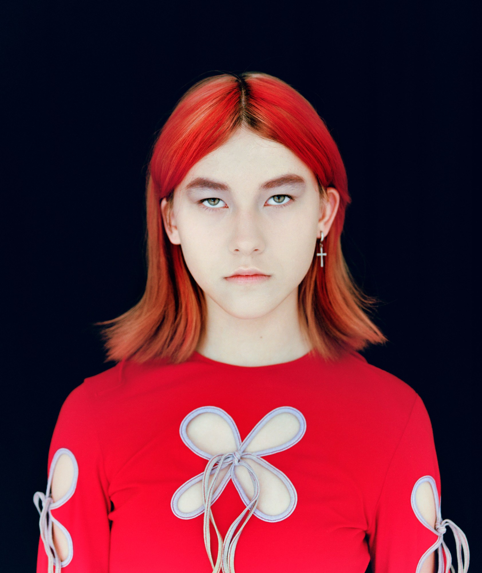 a young girl with red hair wearing a red cutout top in front of a black background