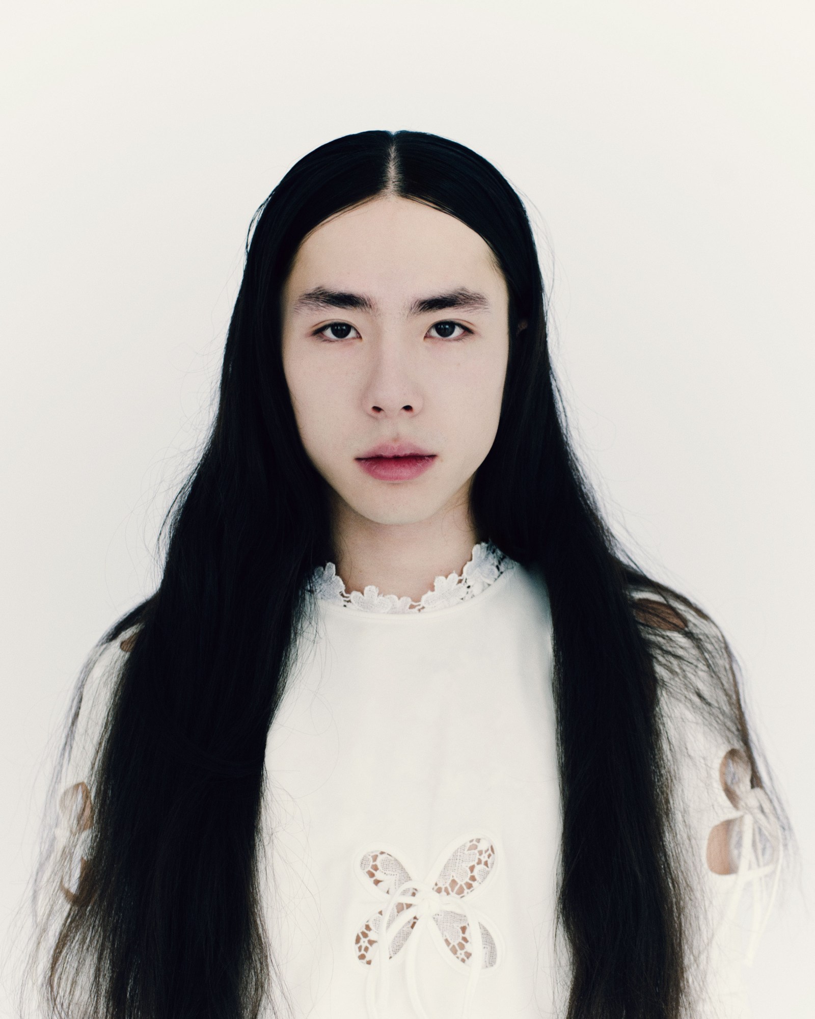 a soviet korean man with long black hair wearing a white lace top