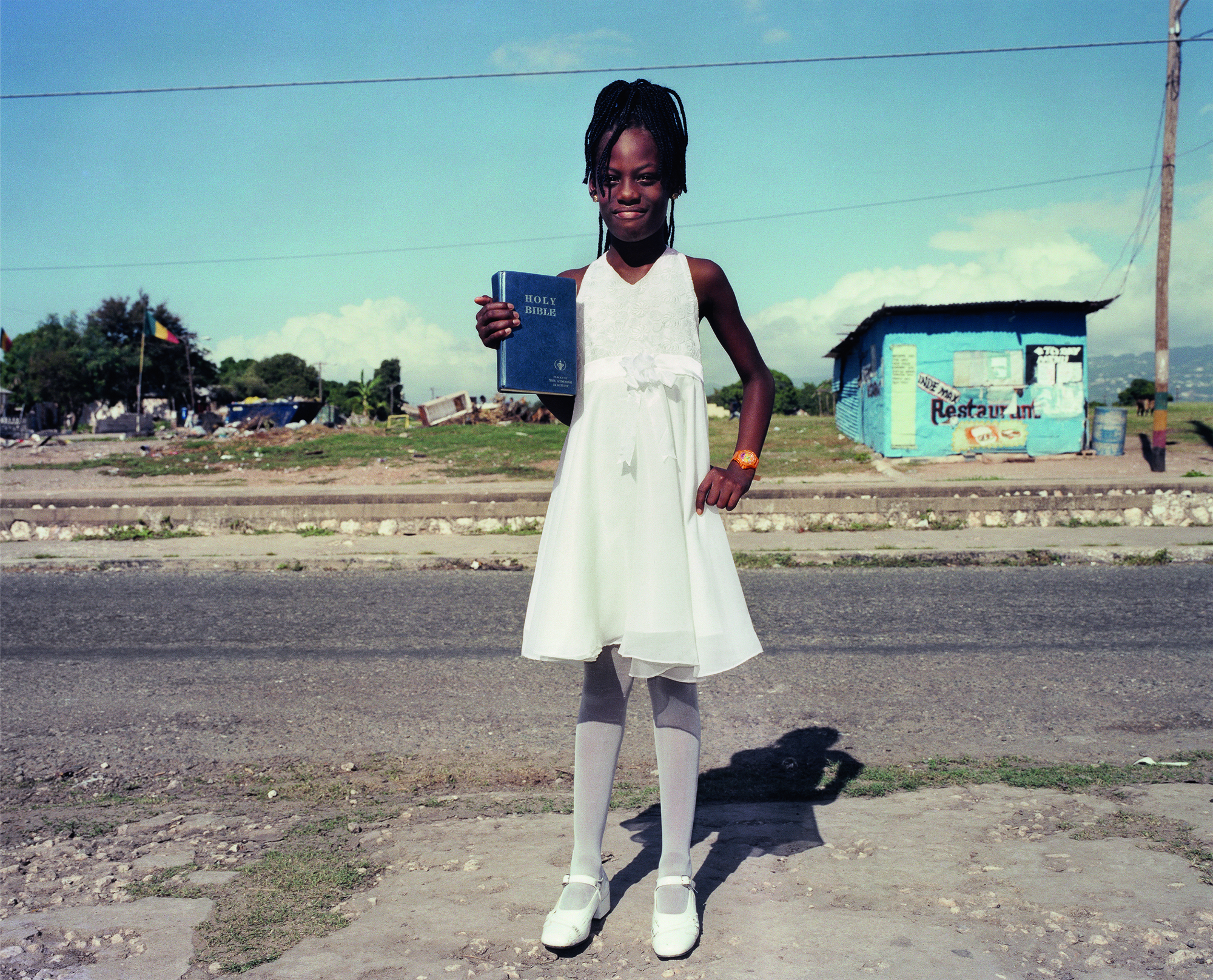 a young girl in a white dress, stockings and shoes, carrying a copy of the bible