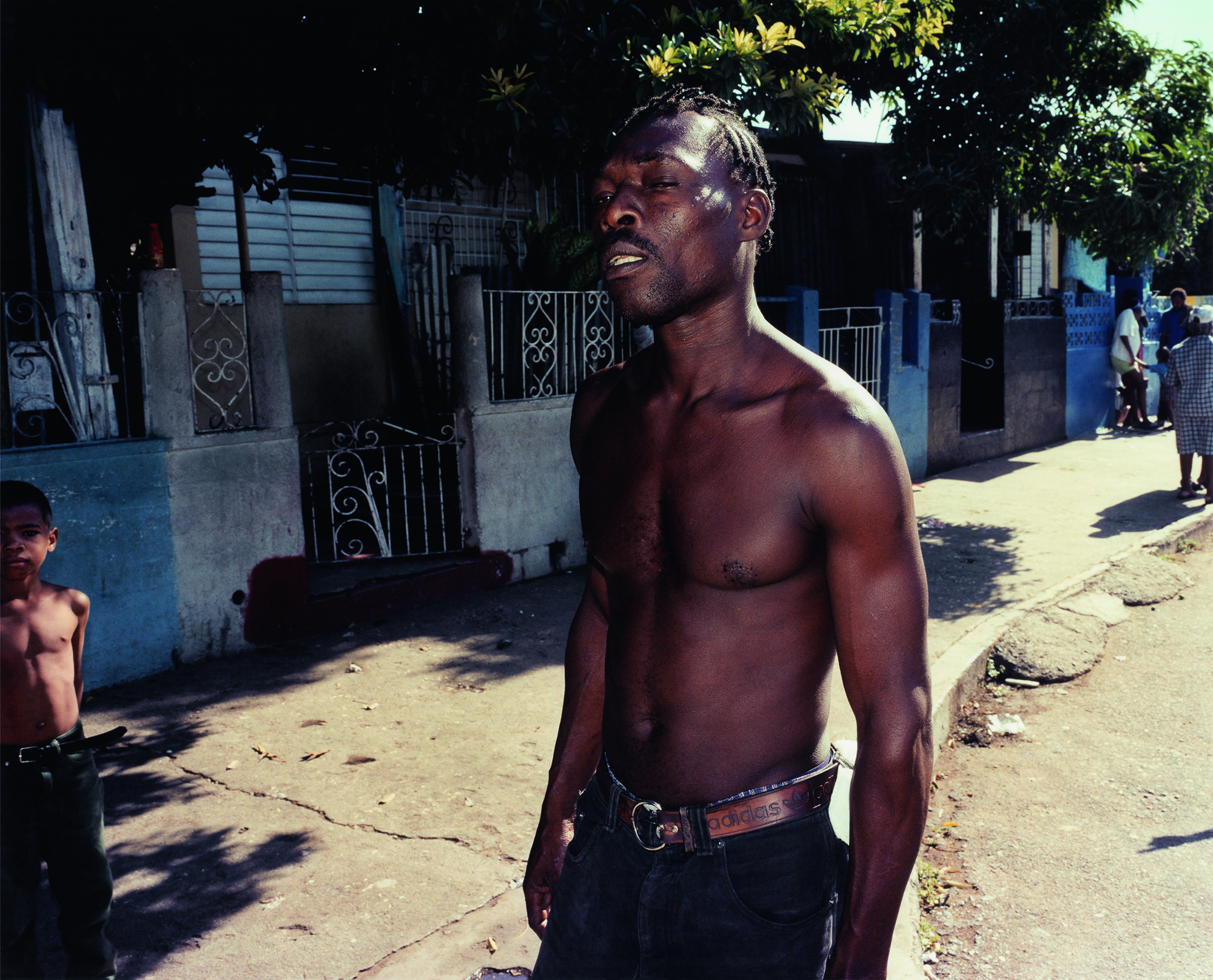 a topless man in dark jeans standing on a sunny street