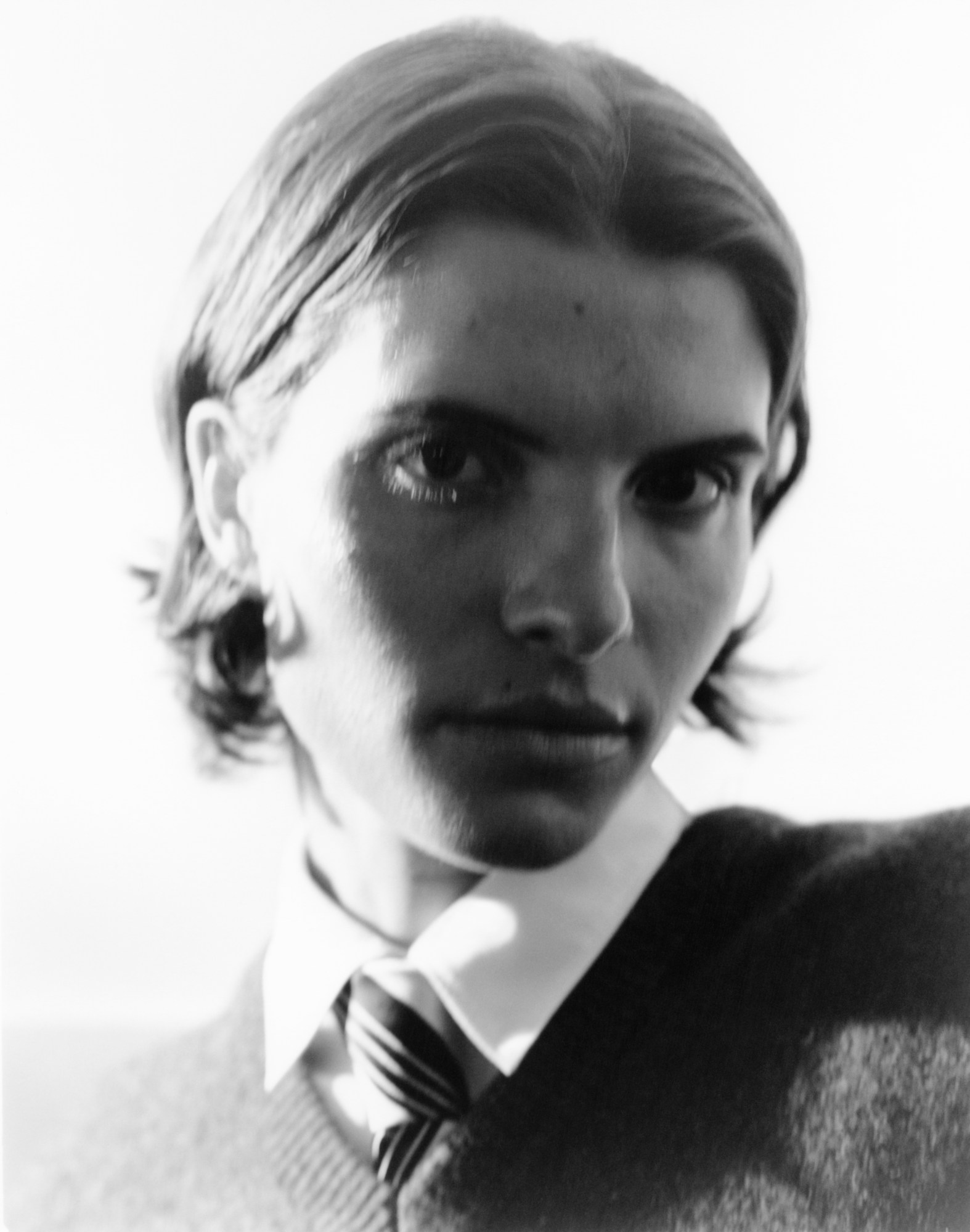 an androgynous model looks into the camera wearing a grey school sweatshirt, shirt and tie