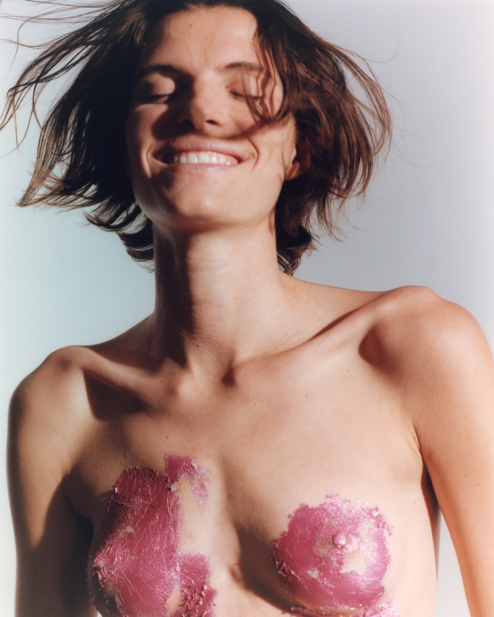 a model smiles with messy hair and dried paint covering her breasts