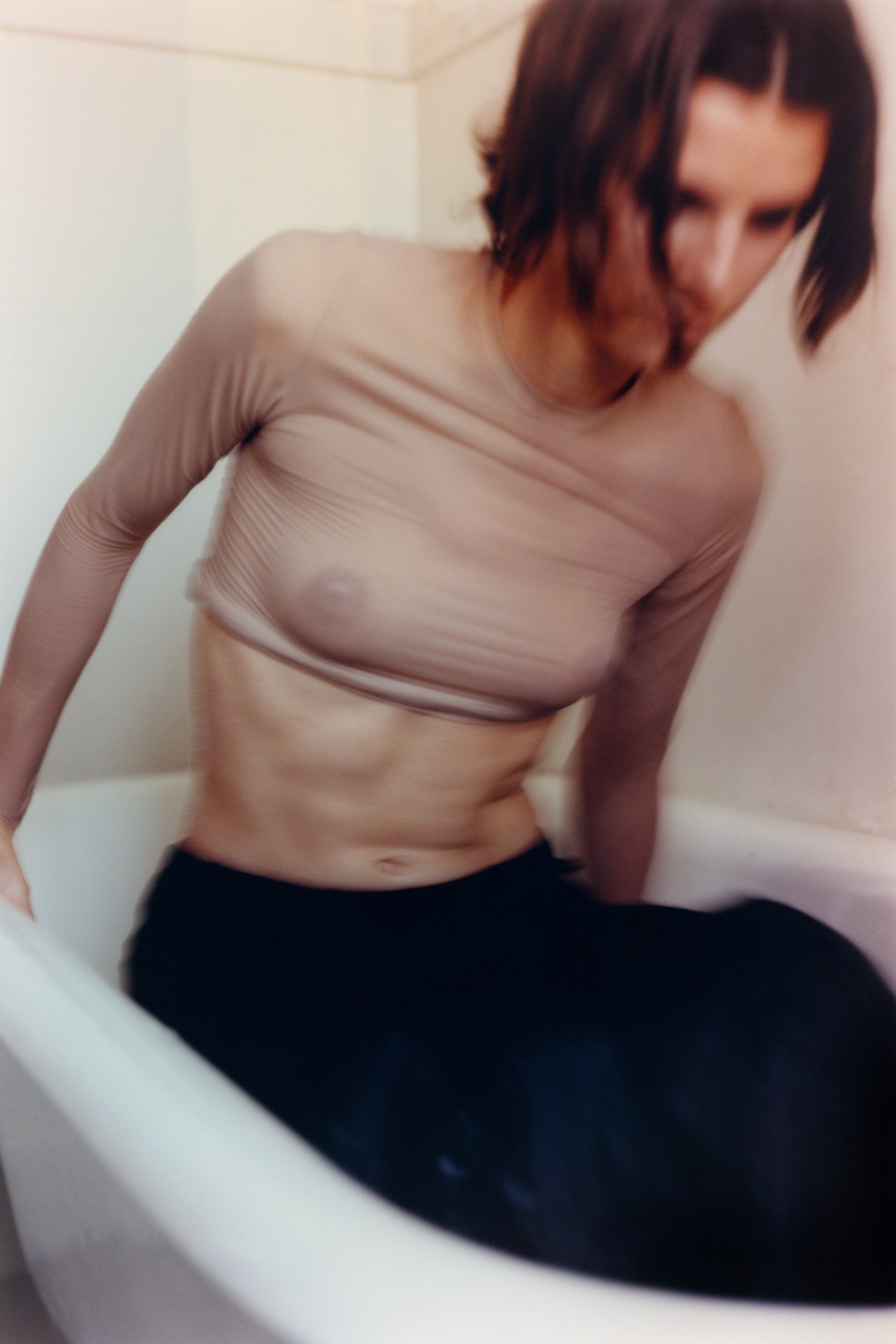 in a blurry shot, a model steps out of a bath wearing a sheer top and long skirt