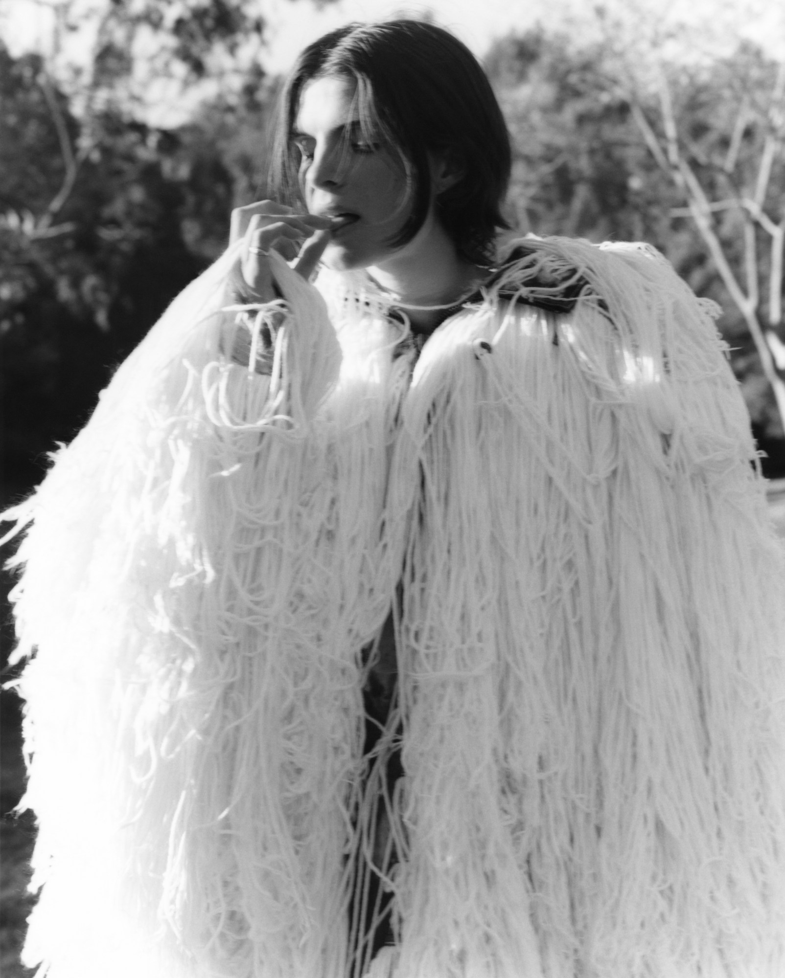 a model wearing a white cape made of strands of wool touches her tongue