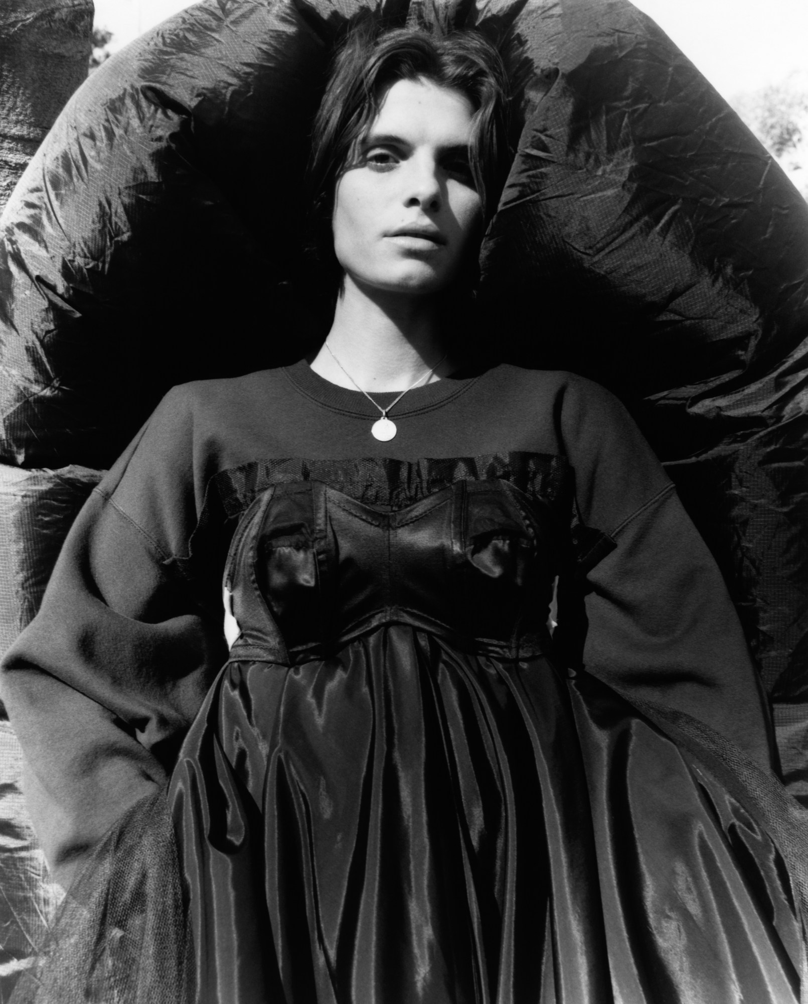 a model in a black dress and sweater looks at the camera with a black blow-up cape behind her