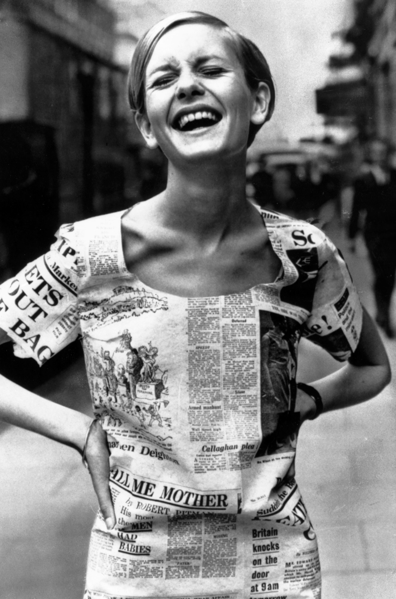 twiggy posing with her hands on her hips and laughing in a newspaper print dress 1967