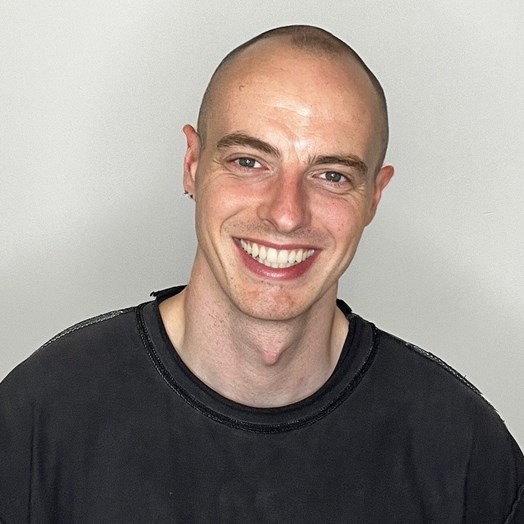 a man in a black t-shirt smiling against a white wall