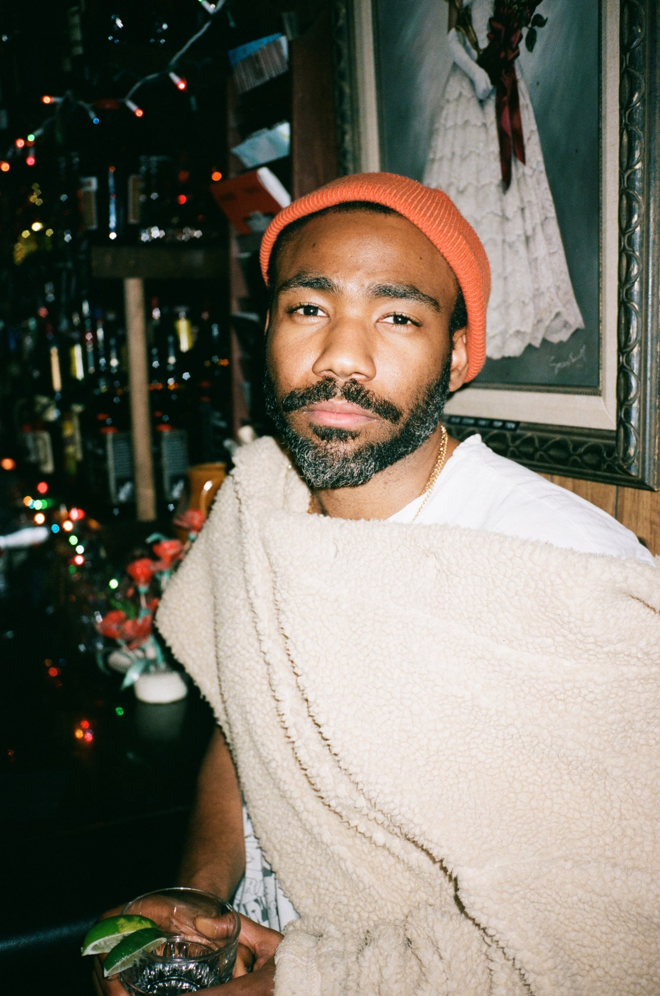 donald glover draped in a shearling blanket, holding a drink with 2 lime wedges on the rim