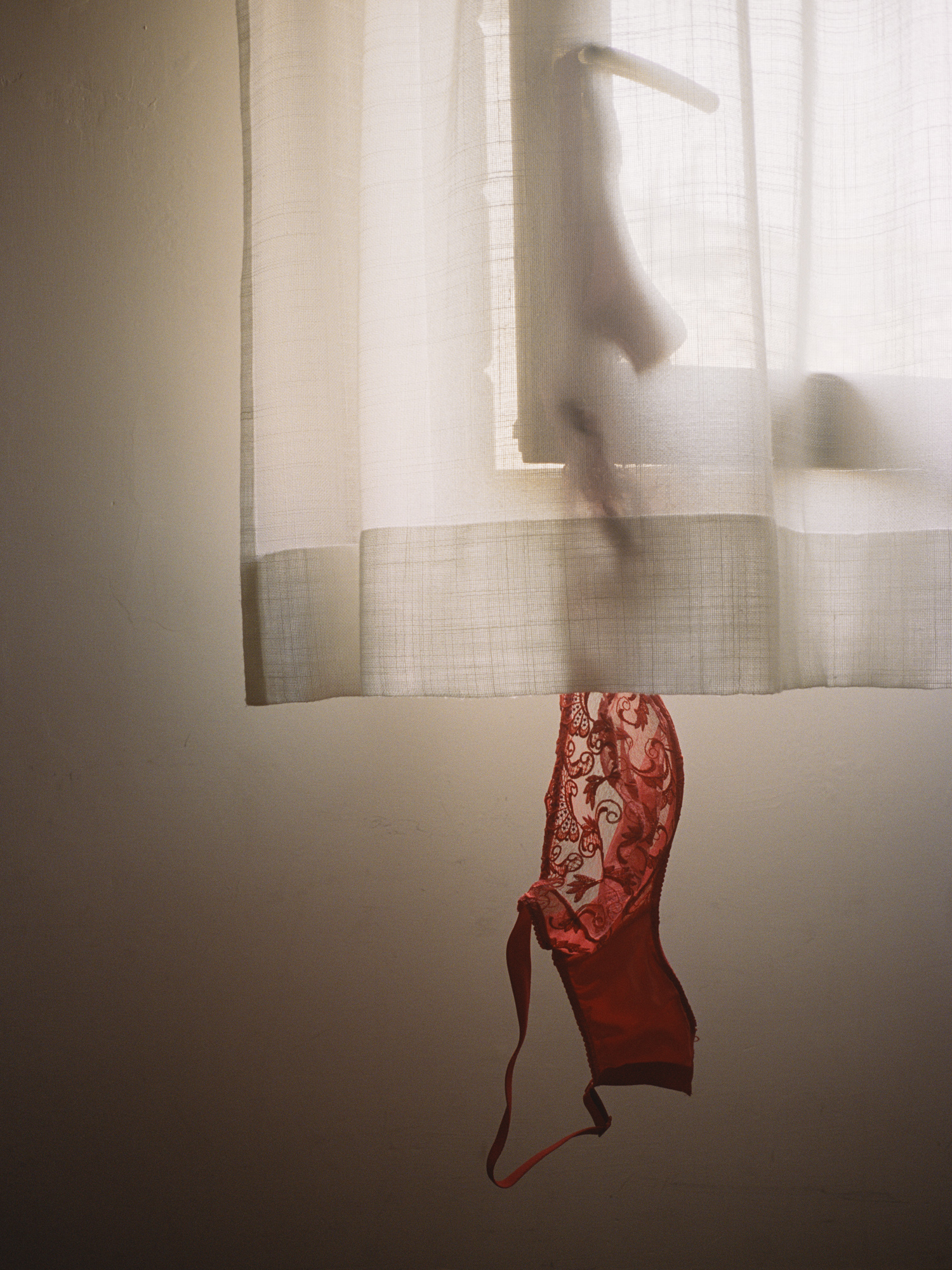 black-and-white photograph by Shaniqwa Jarvis of a bra hanging from a window handle under a curtain