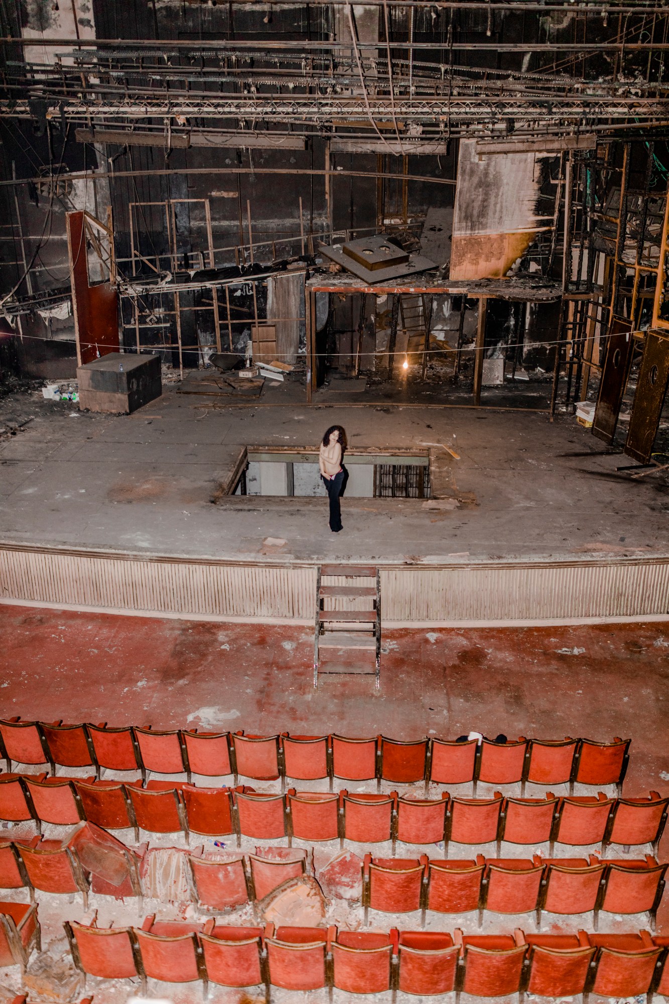 A woman standing on stage in a delapidated theater.