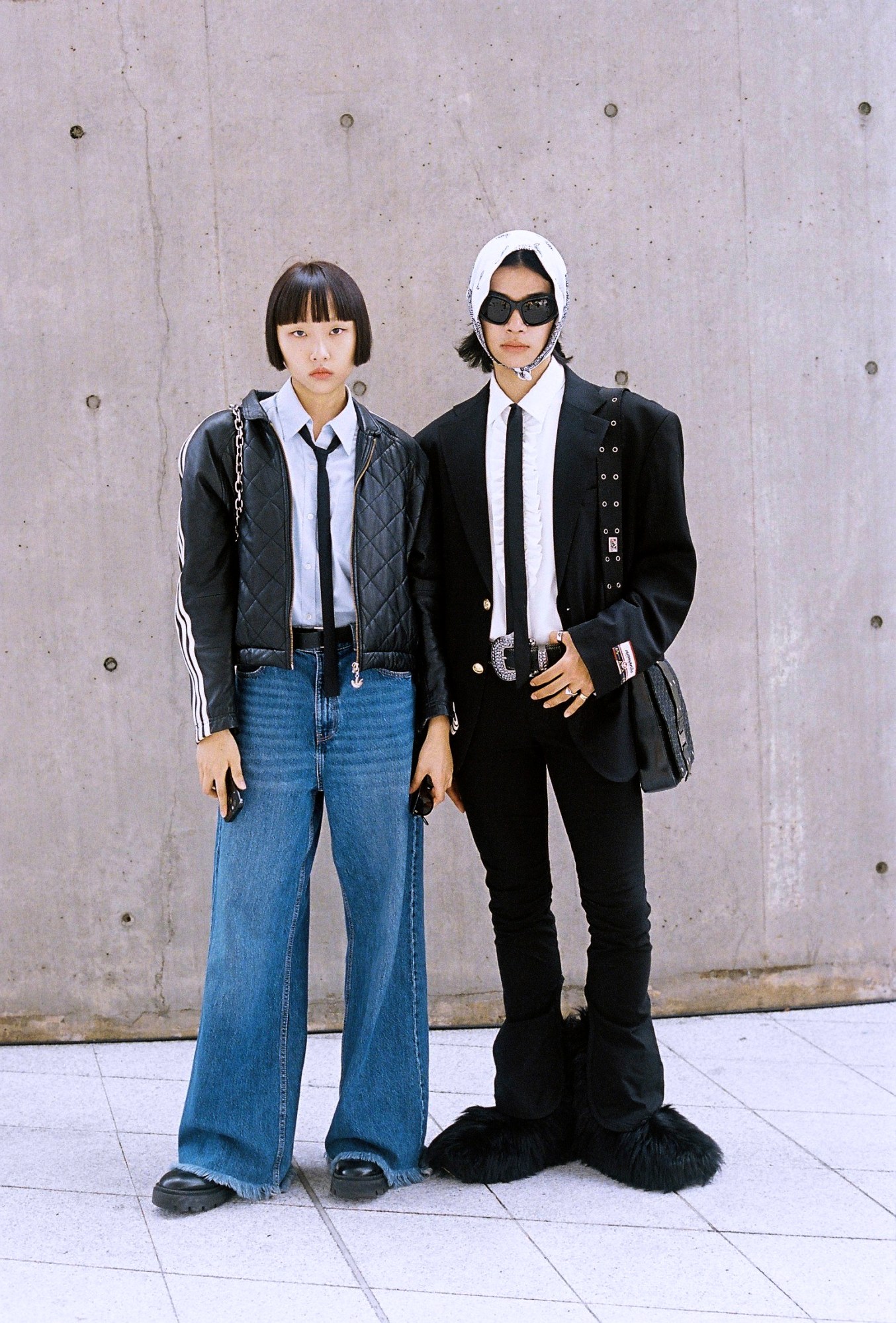 a model couple in matching shirts and ties poses in front of a concrete wall