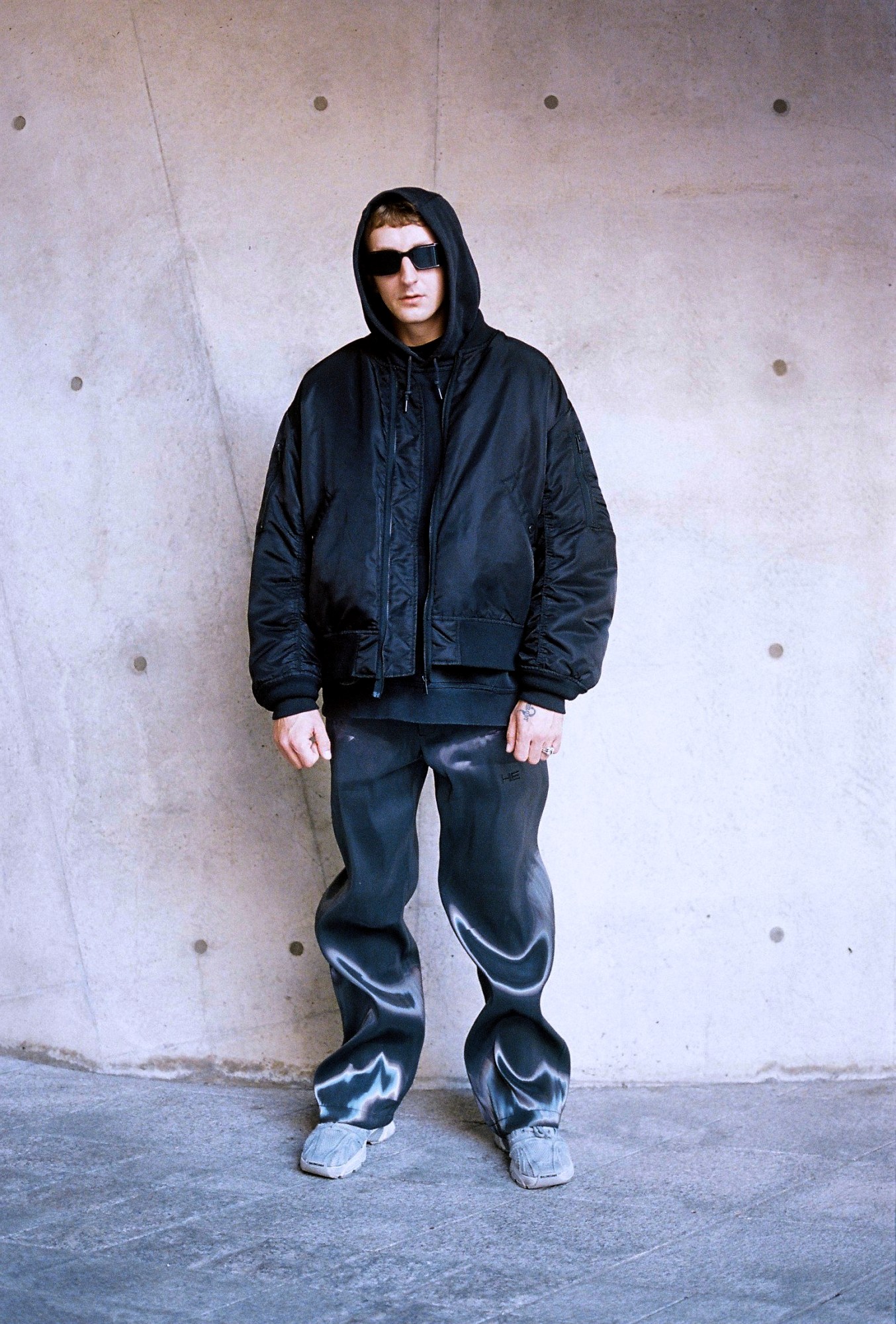 a white man poses in a bomber jacket and wavy trompe de l'oeil trousers