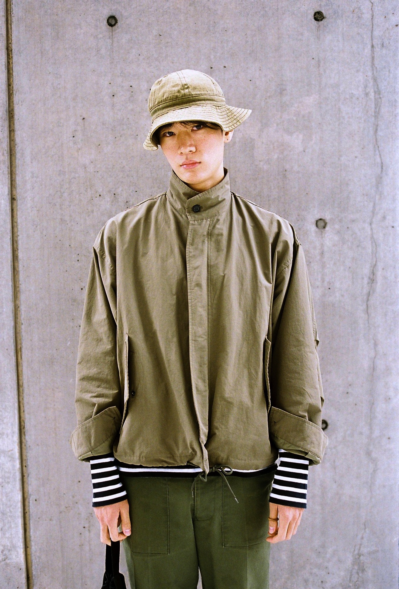 a korean male model wears a green jacket, bucket hat and trousers with striped sleeves