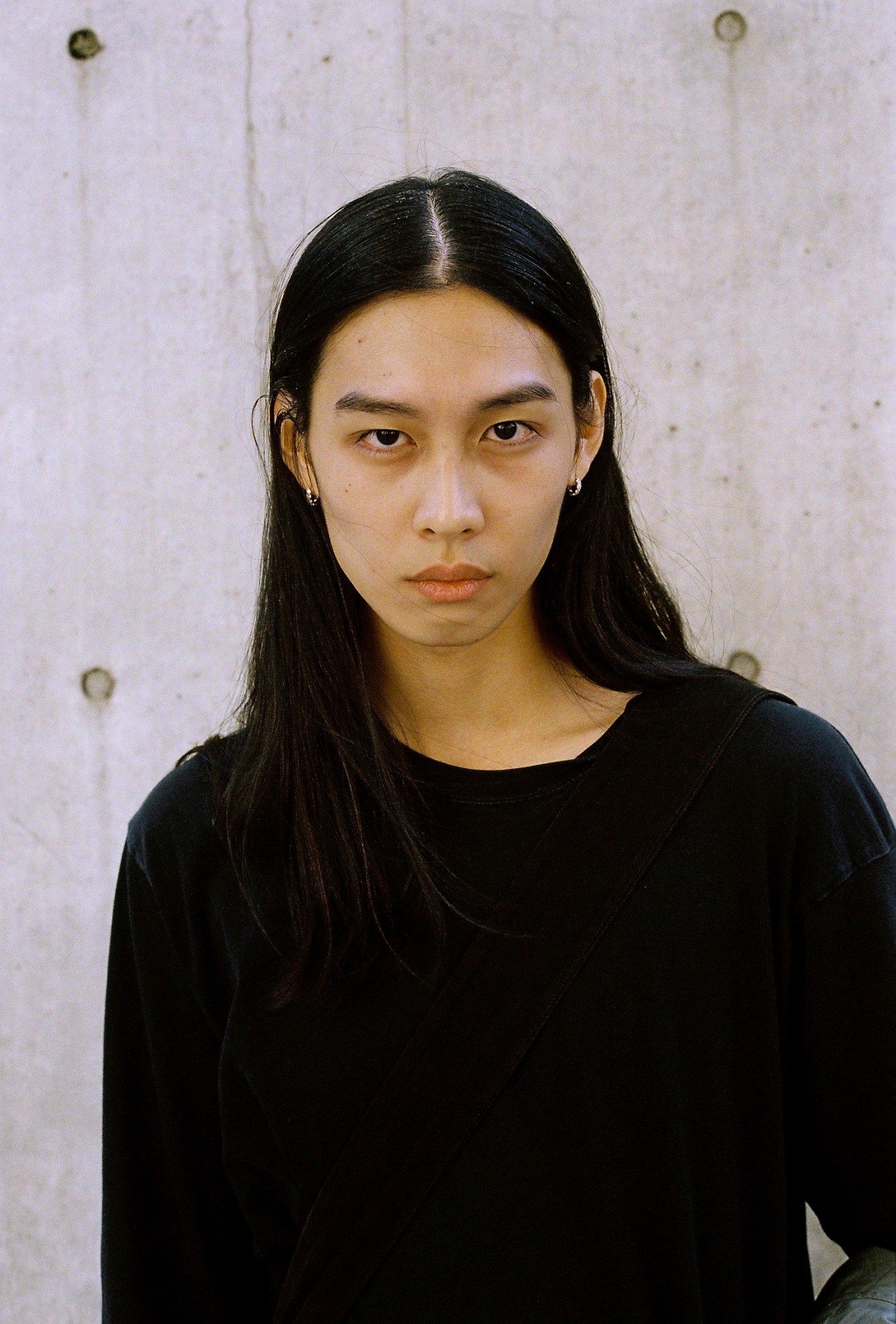 a model with long black hair and small gold hoops poses for a headshot