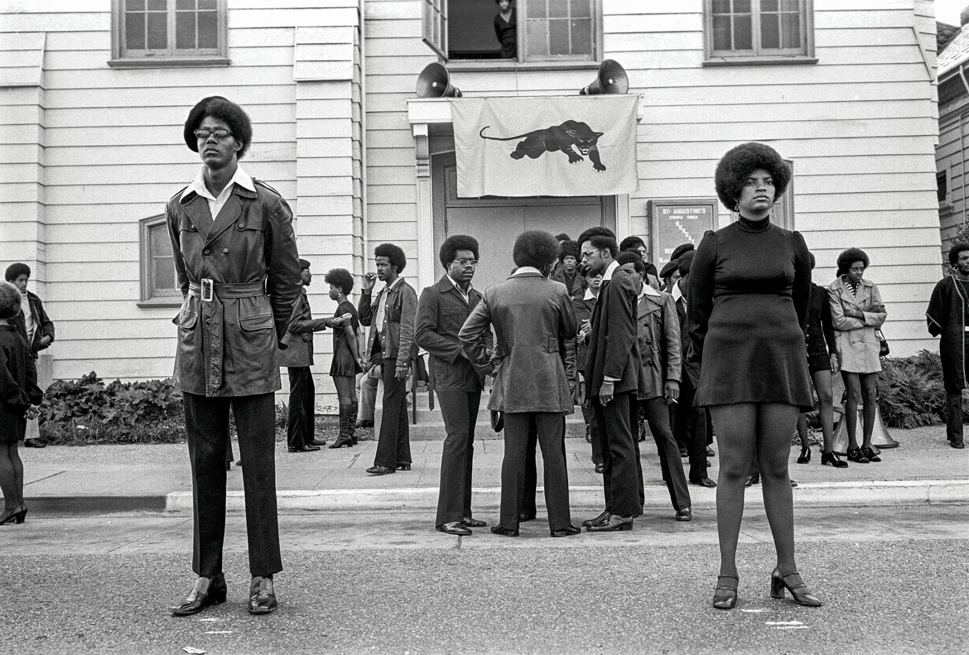 black-and-white photo of the women of the black panther party standing in front of a building with the flag outside