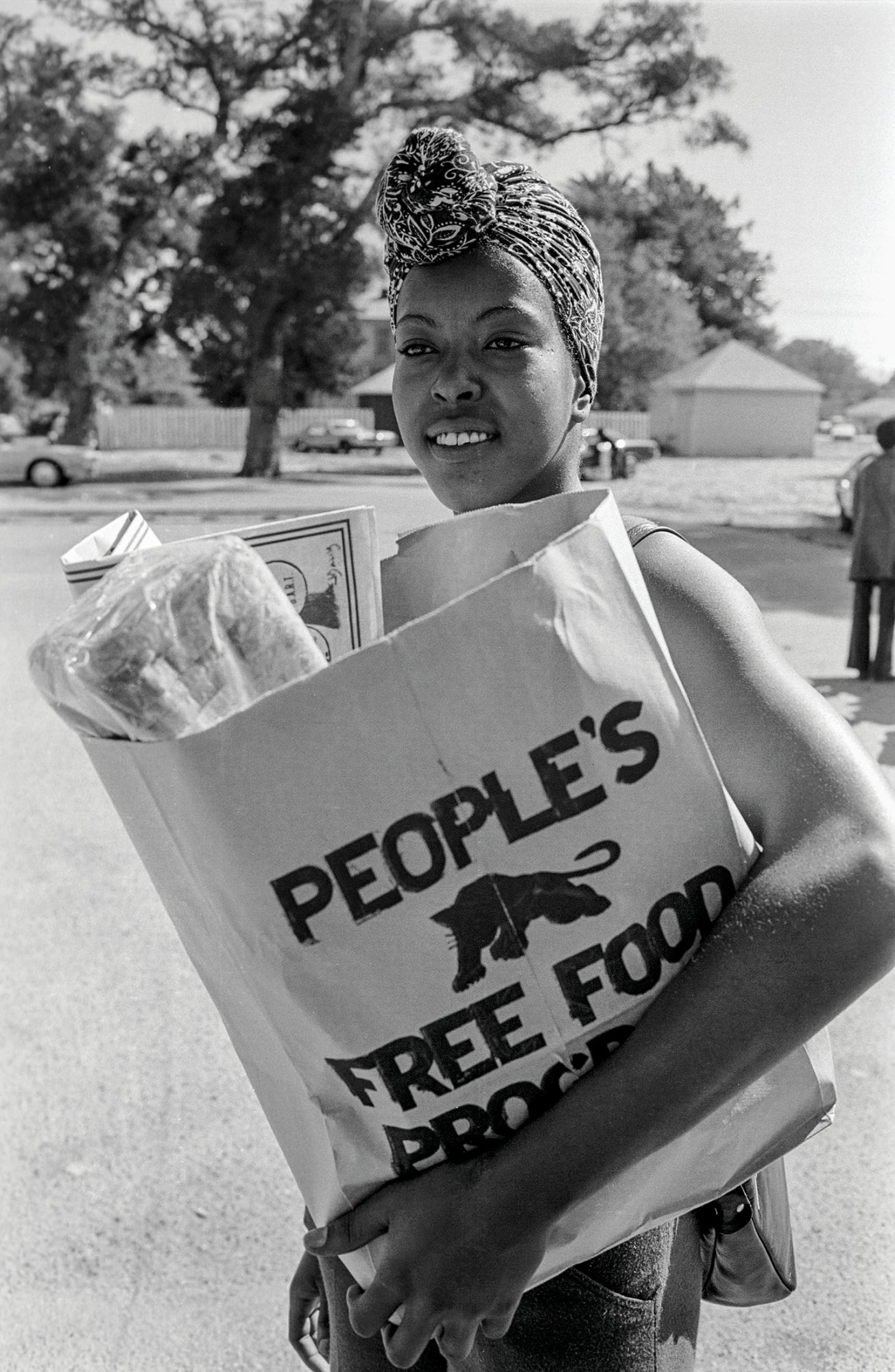 black-and-white photo of a women of the black panther party holding a people's free food program bag filled with food