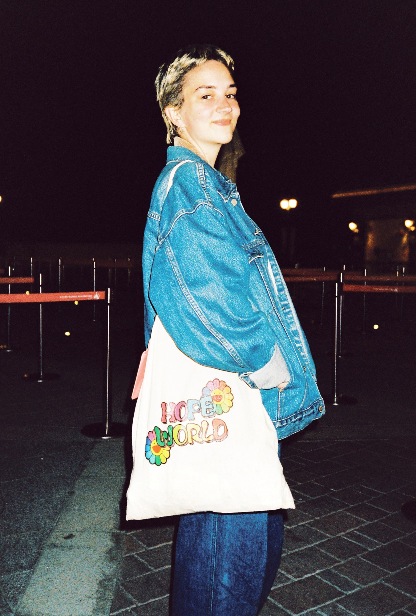 a fan with short bleached hair dressed in all denim looks over their shoulder