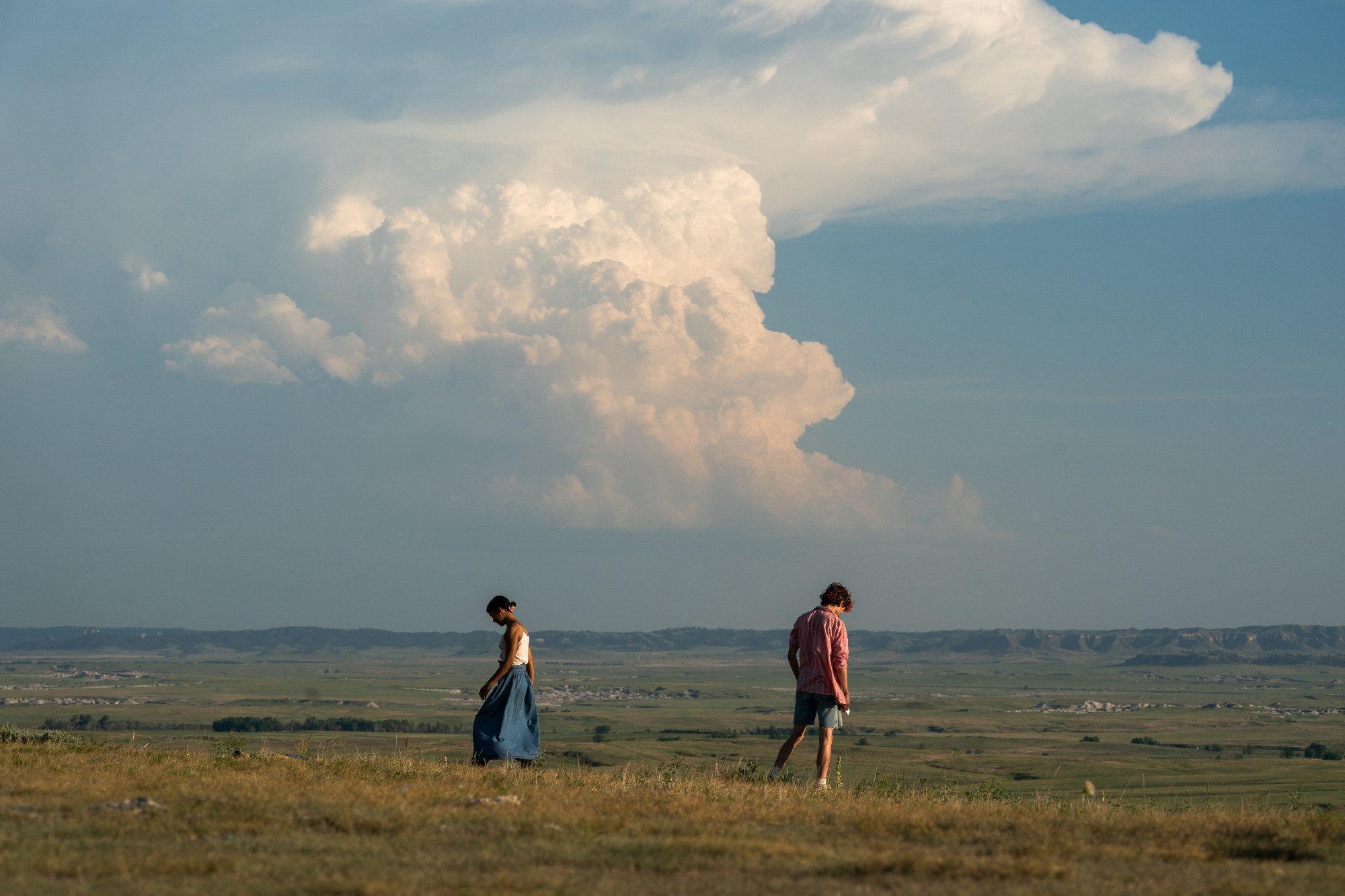 actors facing away from each other in a green field under a blue cloudy sky