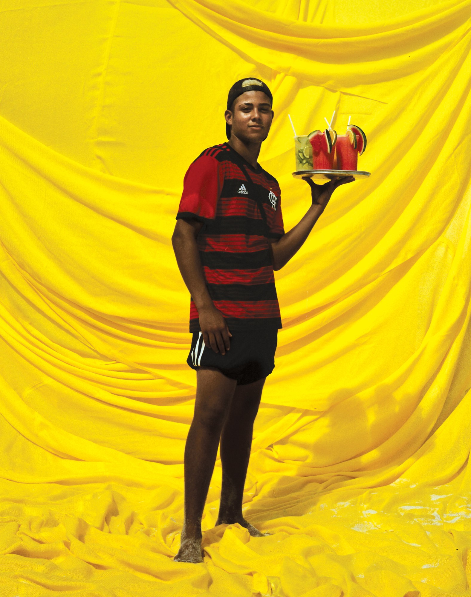 a boy in a soccer kit holding a tray of frozen drinks in front of a yellow backdrop