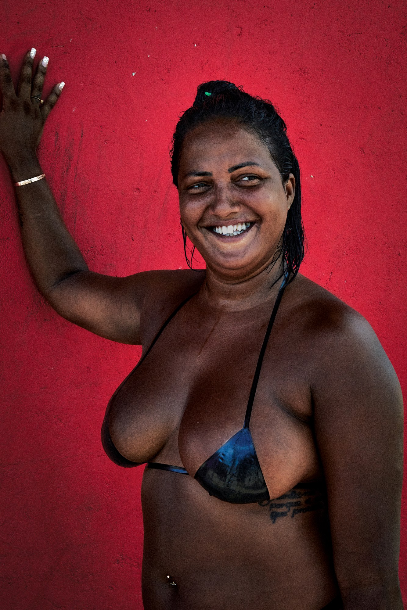 a woman in a black taped bikini leaning against a red wall