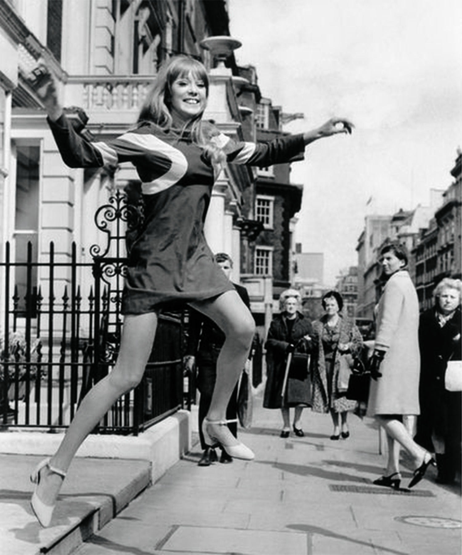 black-and-white image of pattie boyd leaping off steps in the middle of london