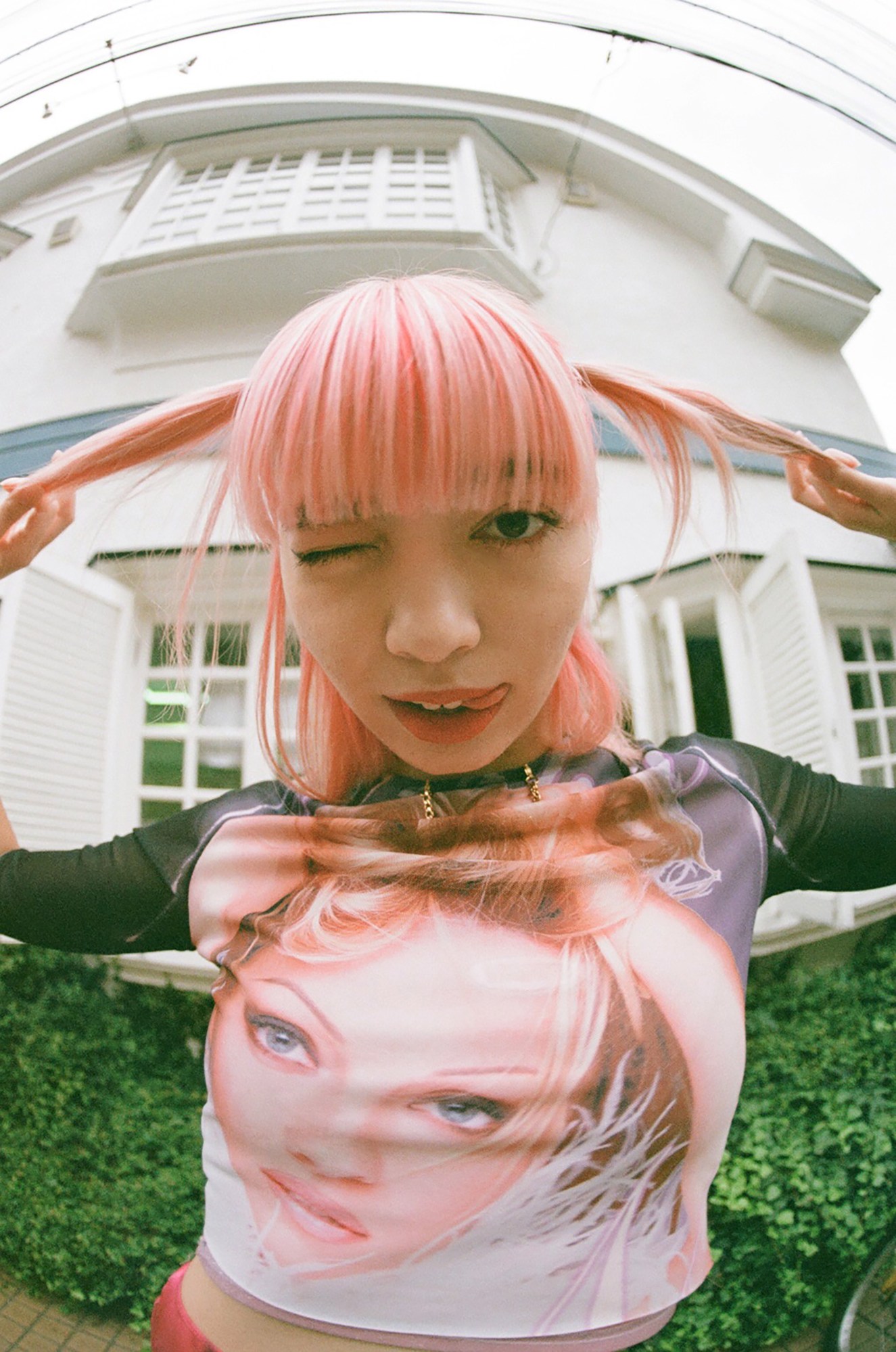 a fish-eye shot of a girl with pink hair sticking her tongue out and winking for the camera