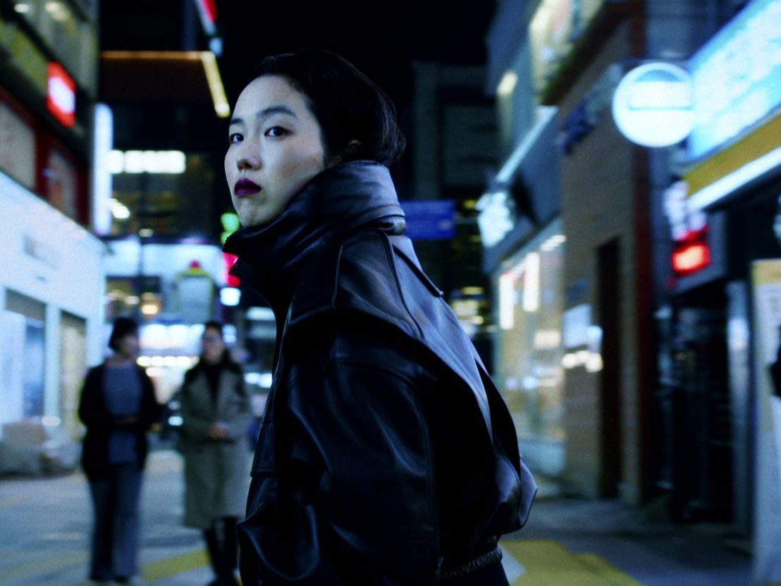 screencap from return to seoul, a woman looking over her shoulder on a bright street at night