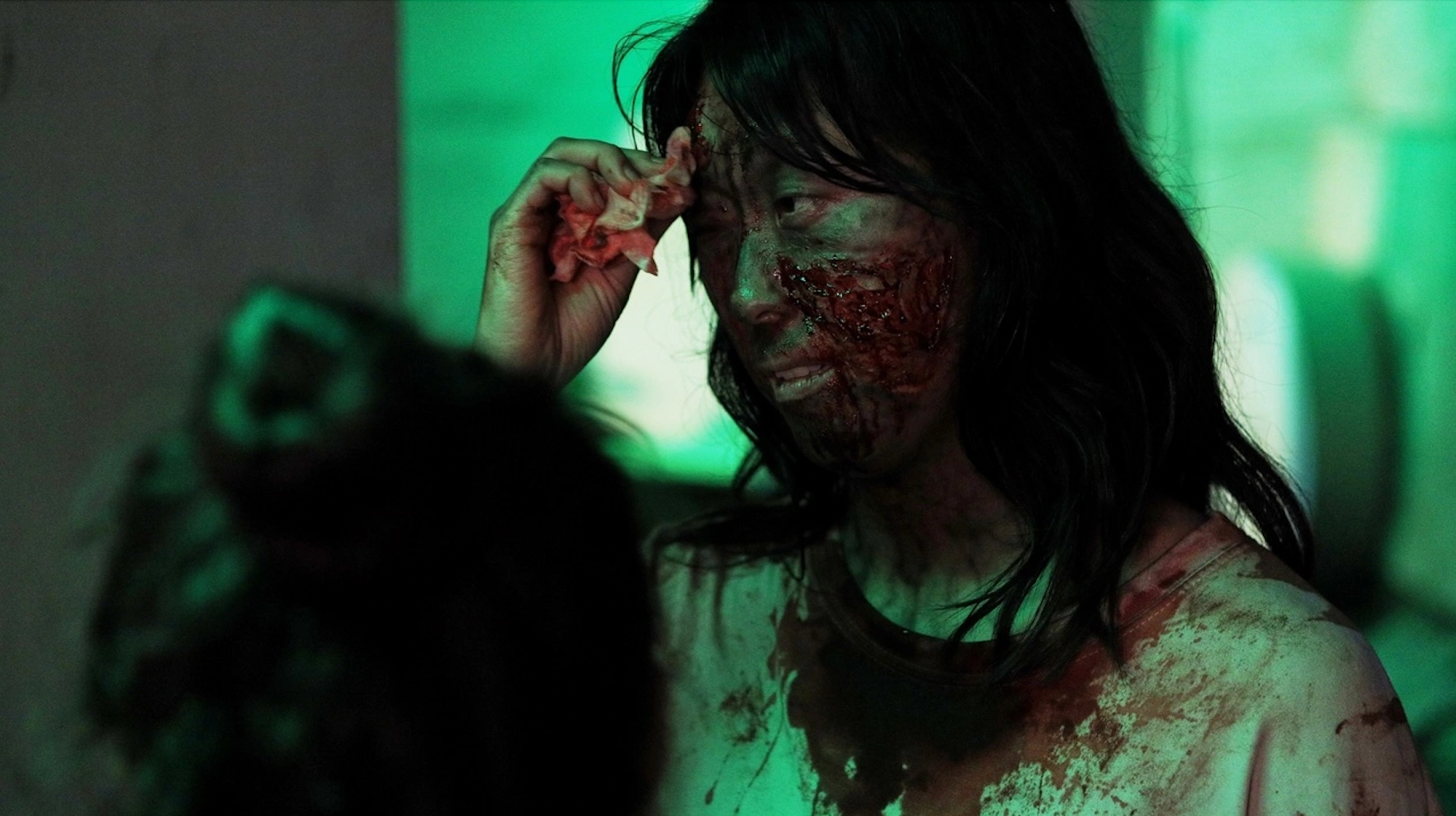 screencap from 29th breath, a woman in zombie make-up against a green lit background